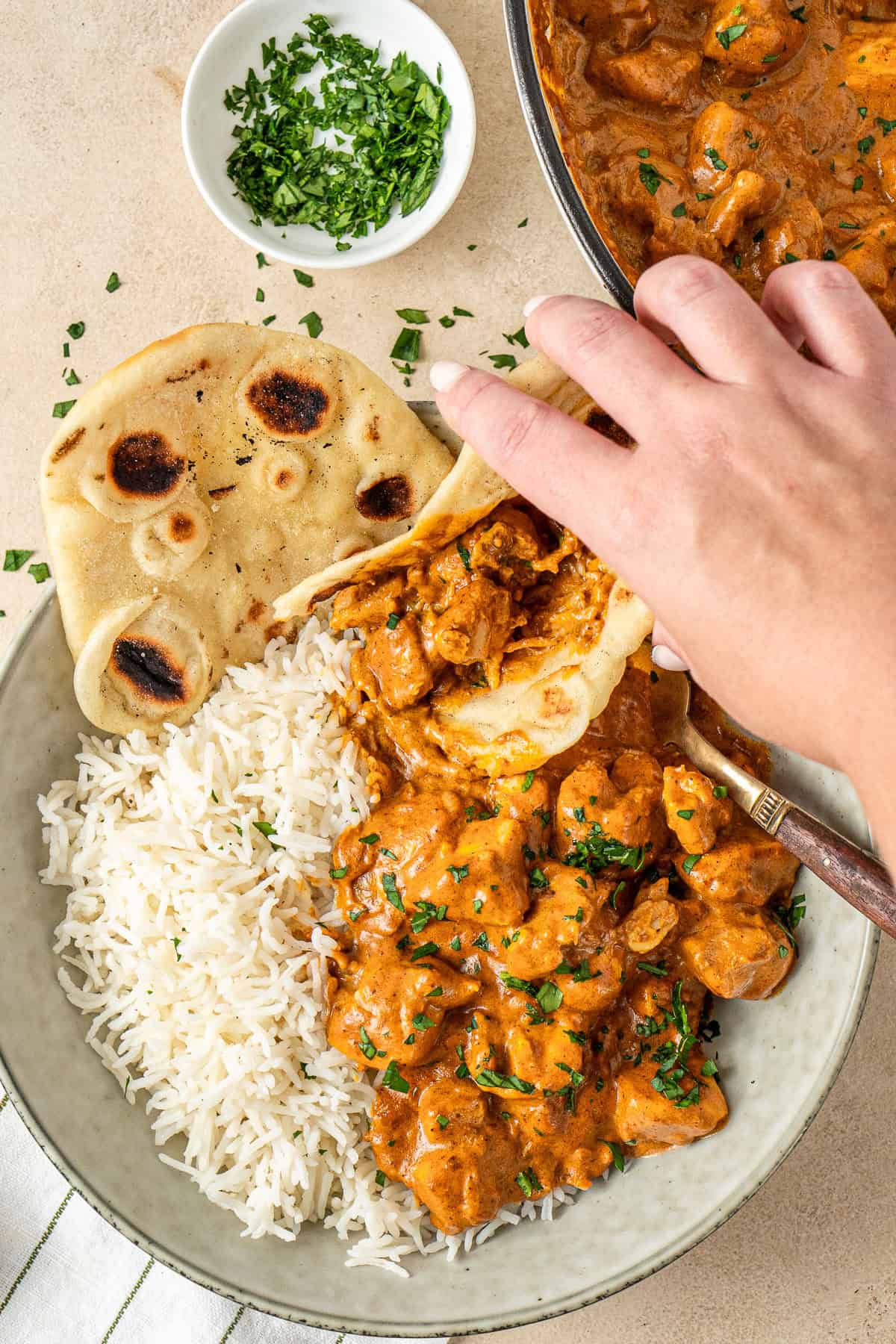 A hand picking up a piece of naan bread with butter chicken.