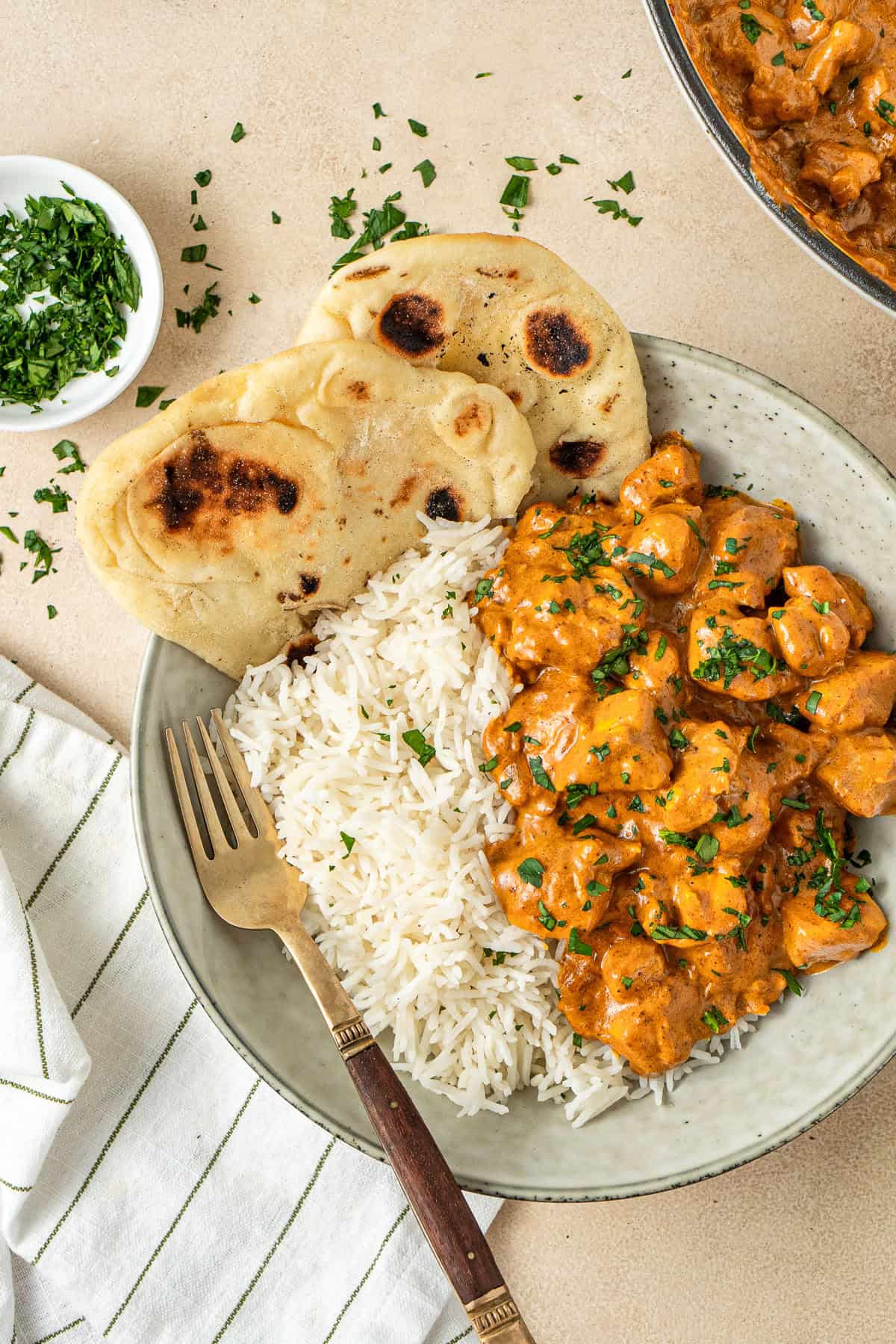 Close up of dairy free butter chicken served with white rice and naan bread and fresh parsley.