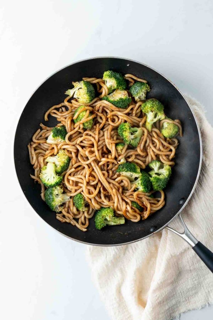 Udon noodles and broccoli cooking in a pan.