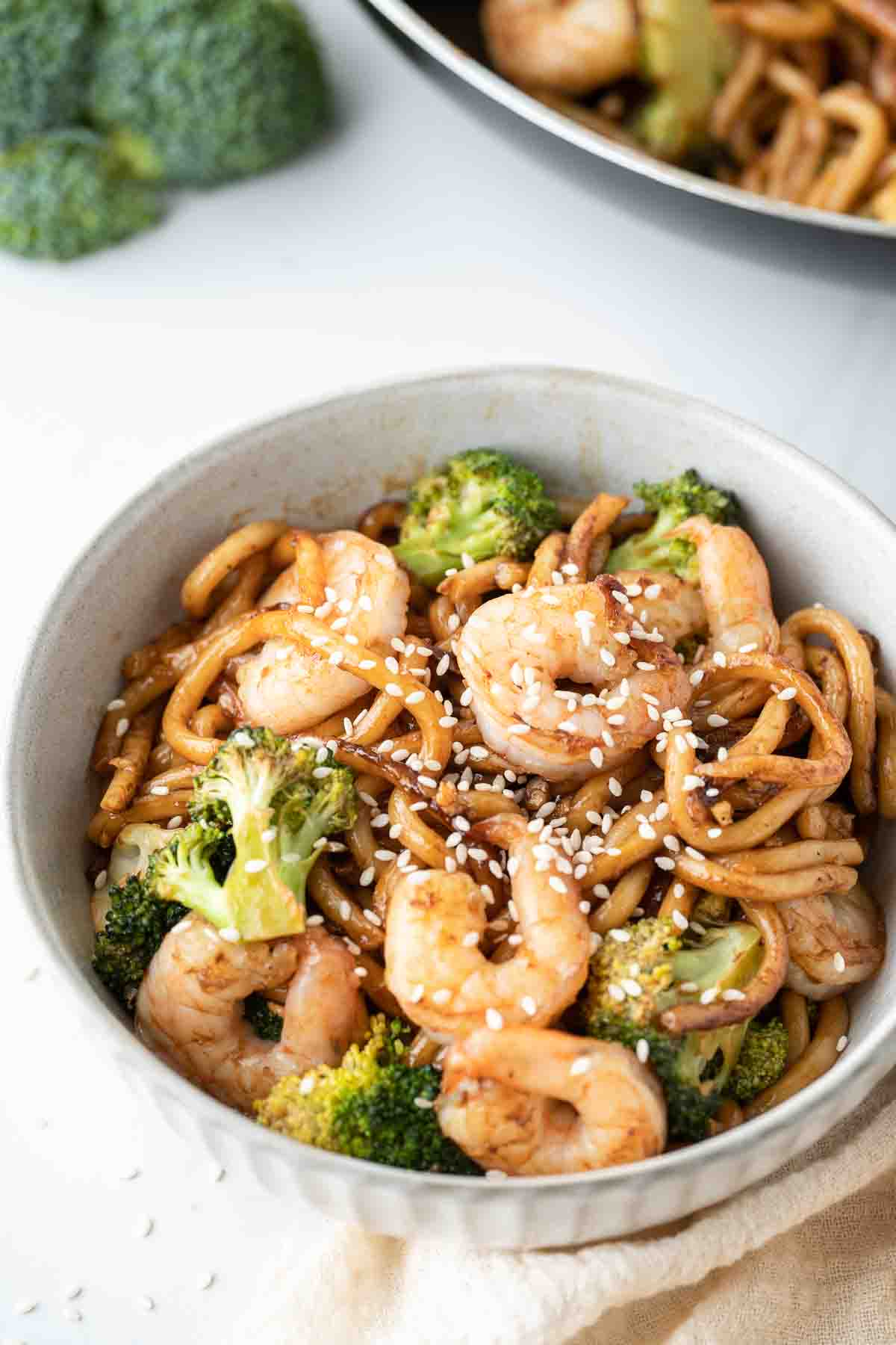 Garlic prawn noodles with sesame seeds in a white bowl.