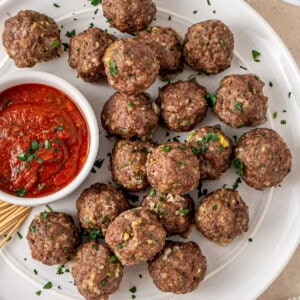 Baked beef meatballs on a white plate with marinara sauce.