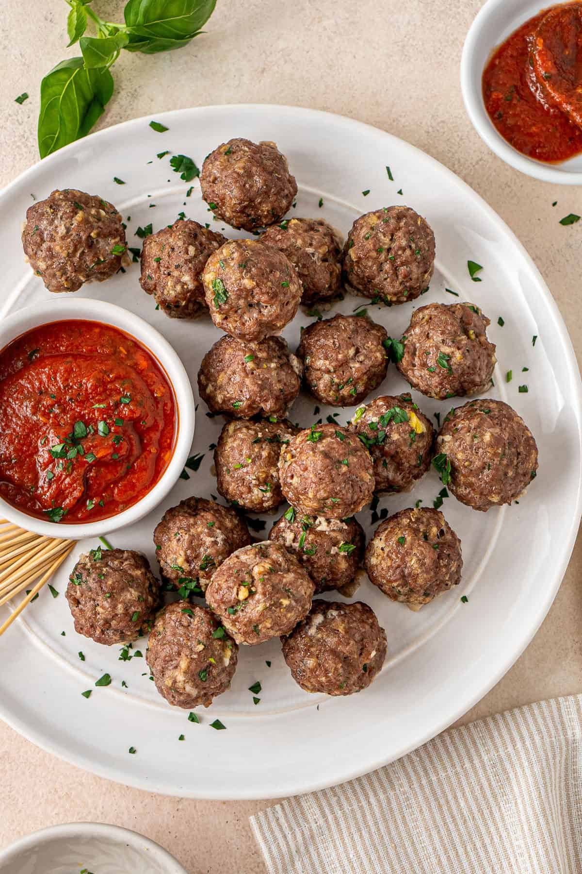 Baked beef meatballs on a white plate with marinara sauce.
