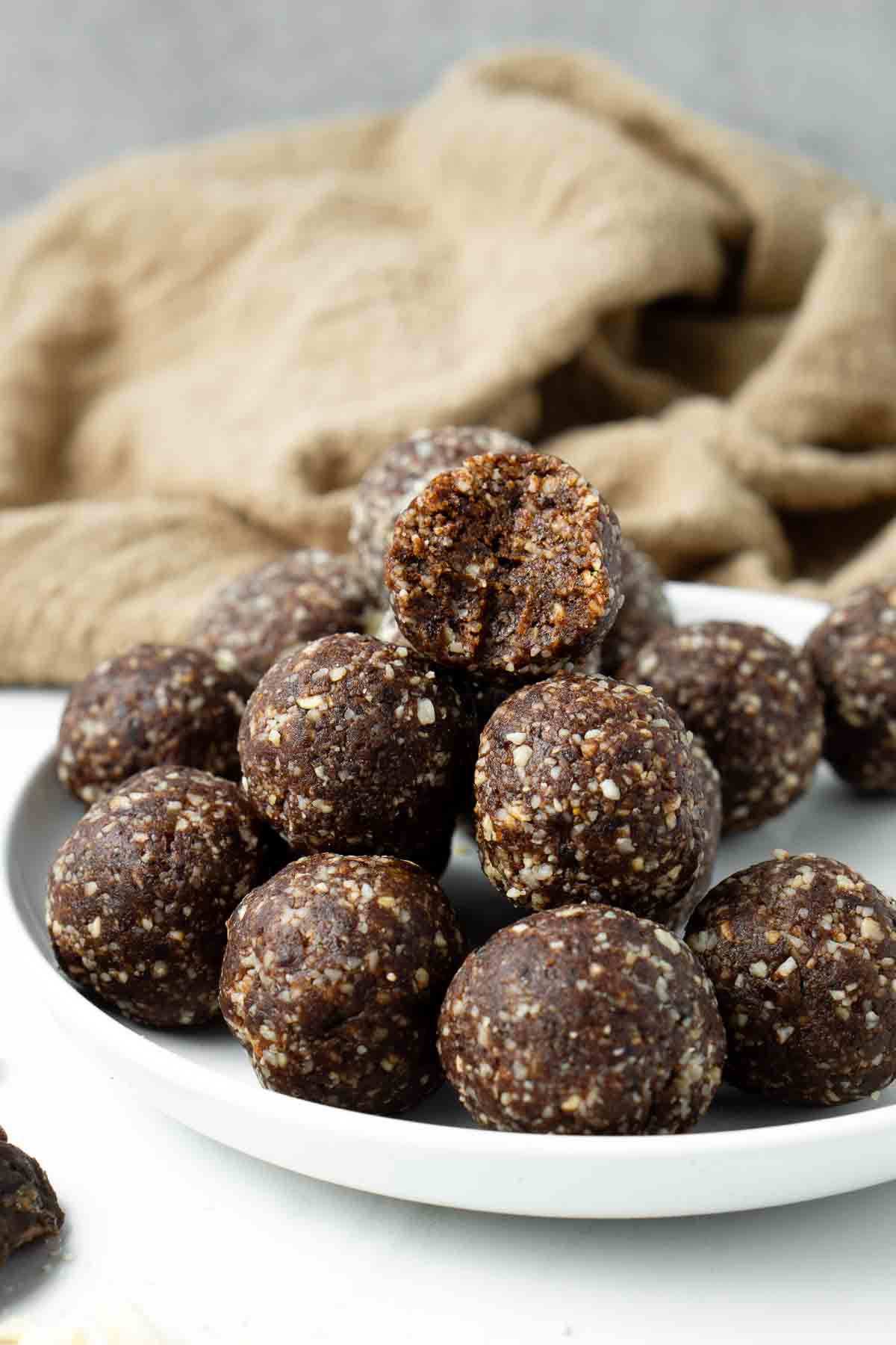 Chocolate Hazelnut Bliss Balls in a pile on a plate with one having a bite taken out.