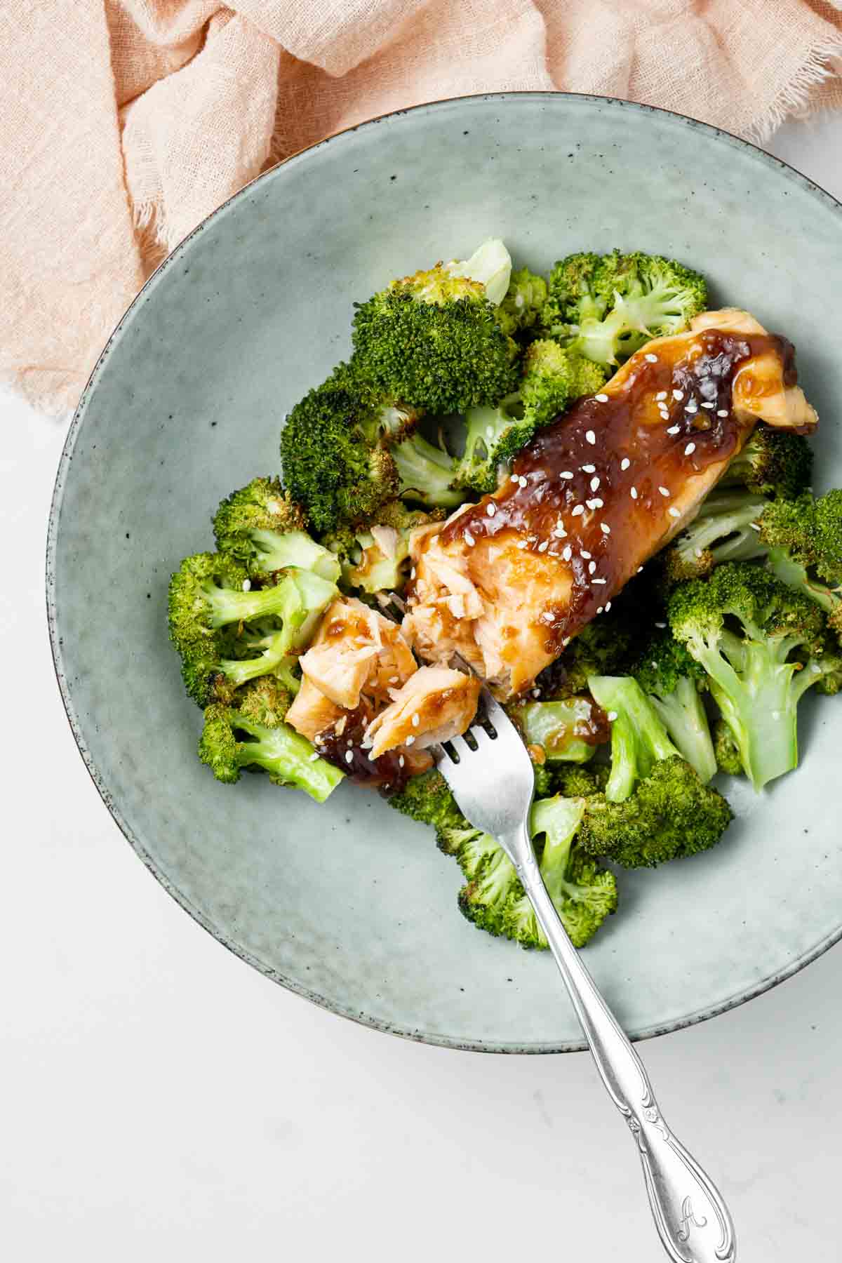 A fork breaking apart a salmon fillet with maple glaze on a bed of broccoli. 