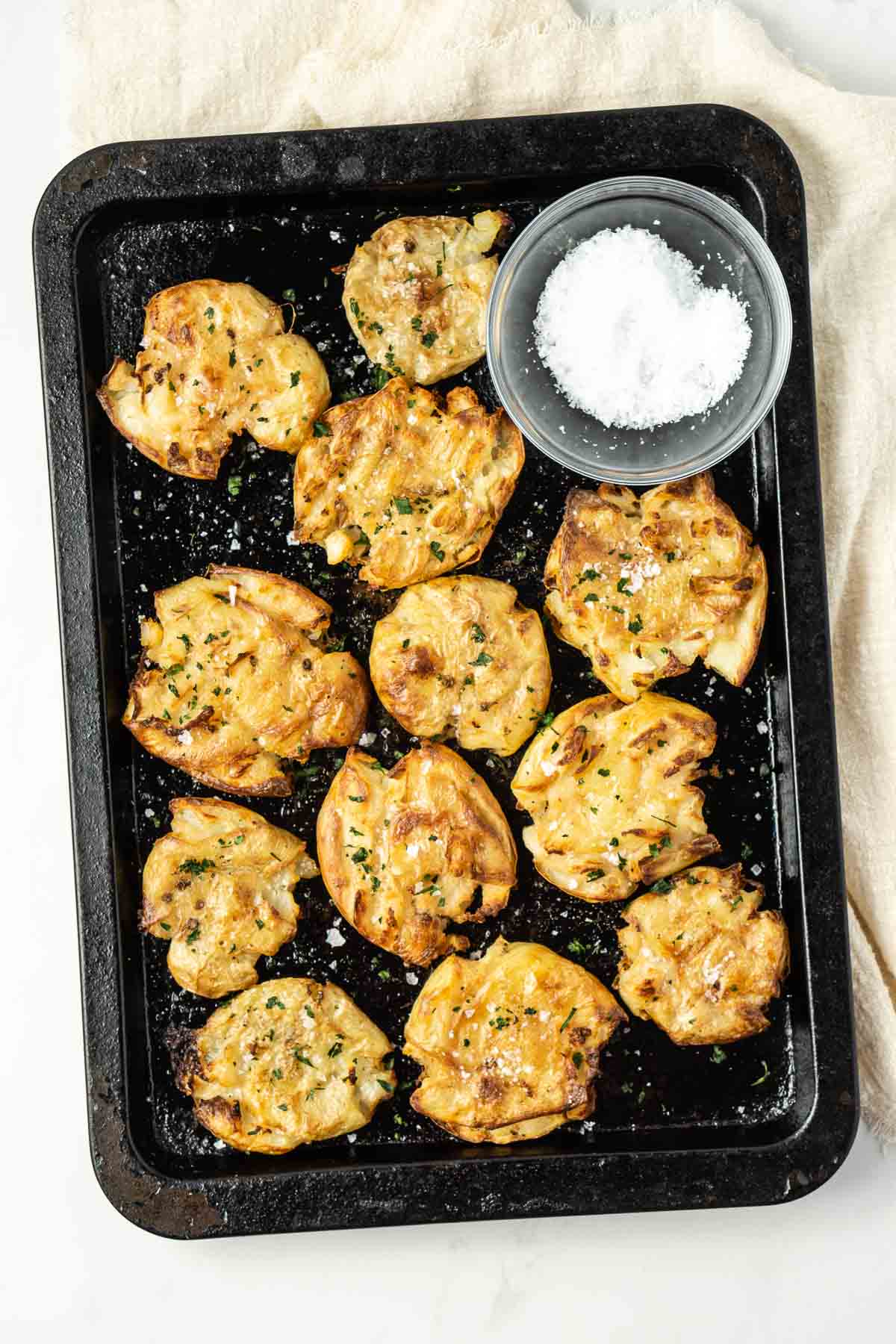 Crispy salt and vinegar potatoes on a baking tray with flaky sea salt