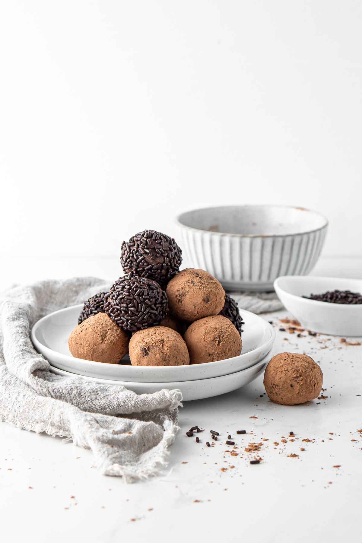 Vegan chocolate truffles served on a white plate coated in chocolate sprinkles and cocoa powder. 