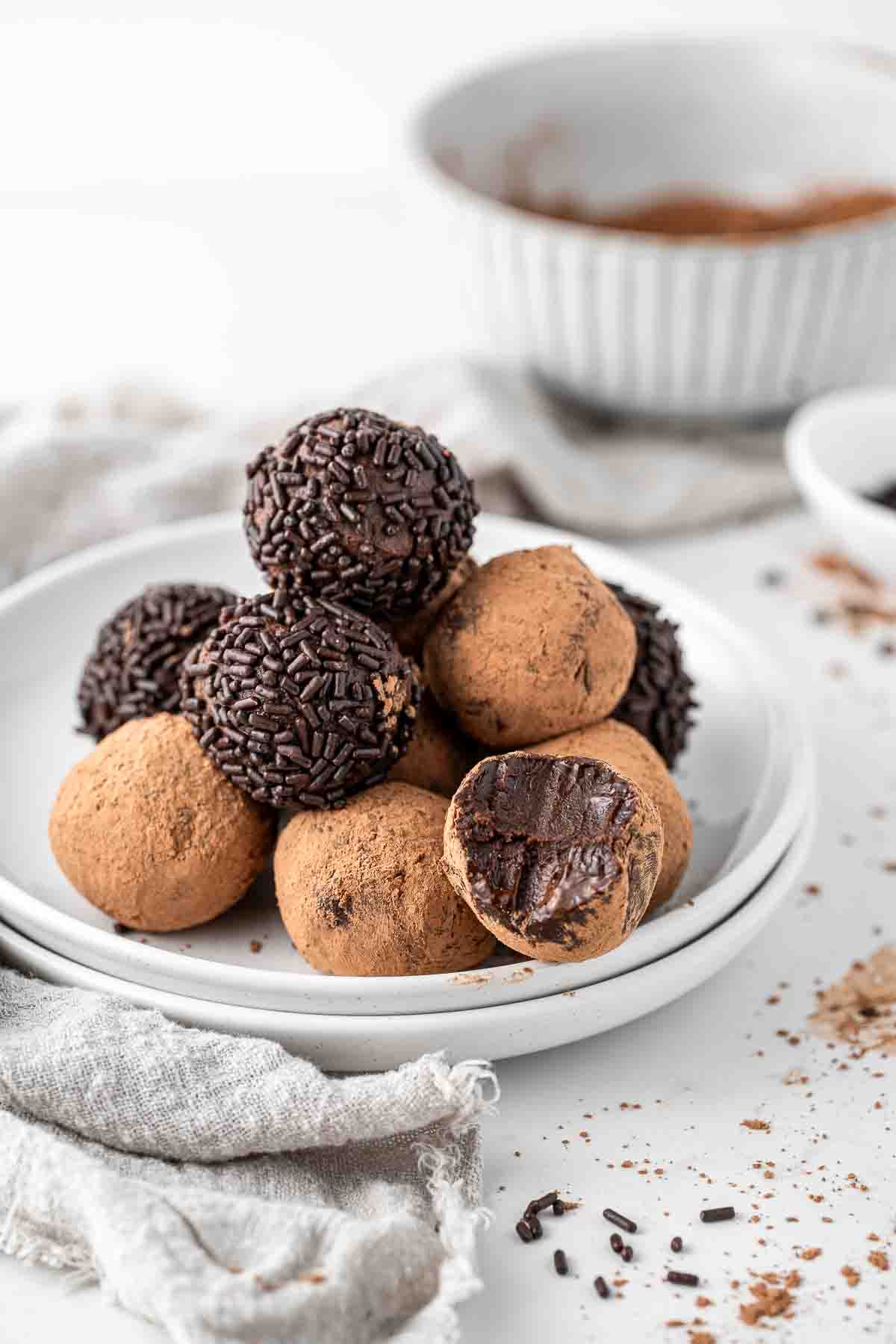 Vegan chocolate truffles on a plate coated in chocolate sprinkles and cocoa powder with a bite taken.. 