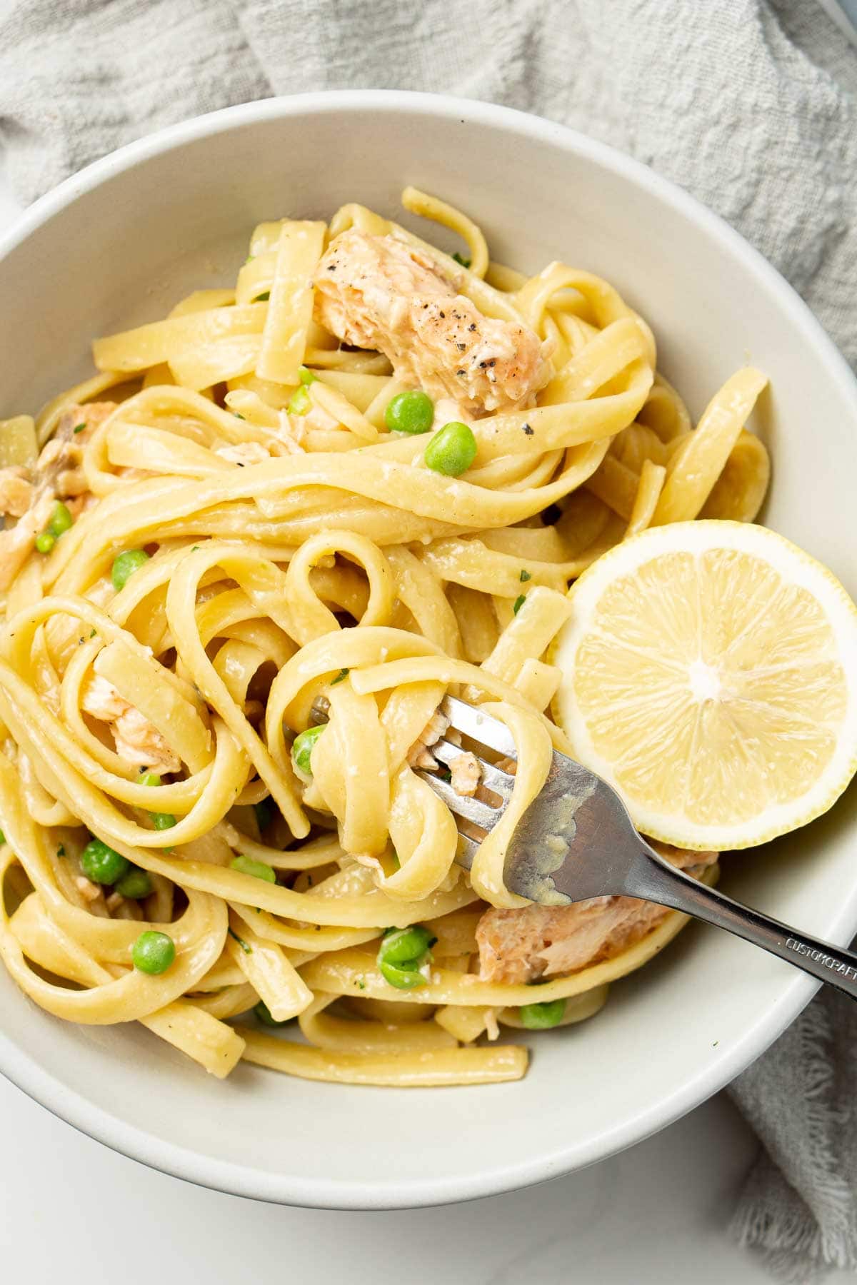 Close up of cream coloured bowl of pasta with lemon slice and pasta twirled around a fork.