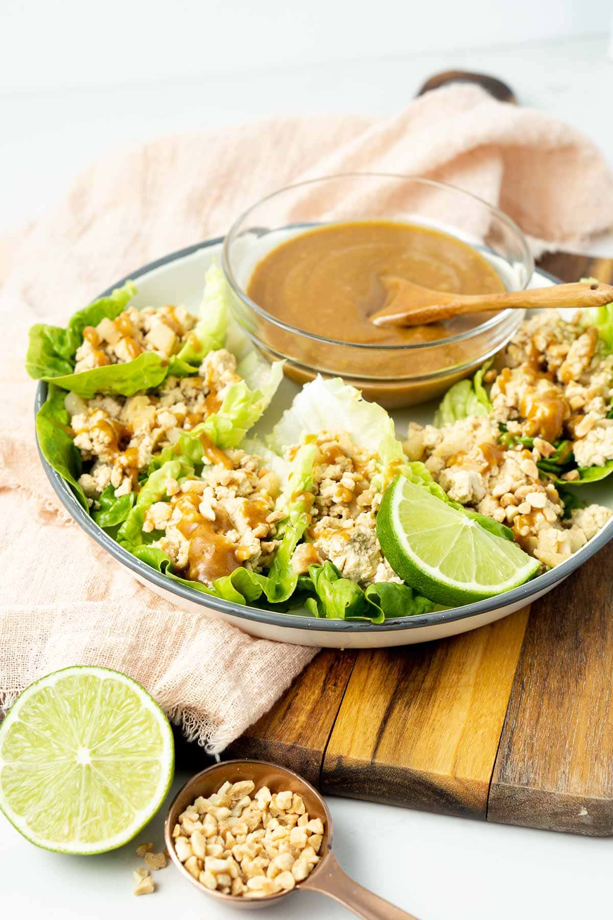Tofu lettuce cups on a plate on a wooden board with a bowl of peanut dipping sauce and fresh limes.