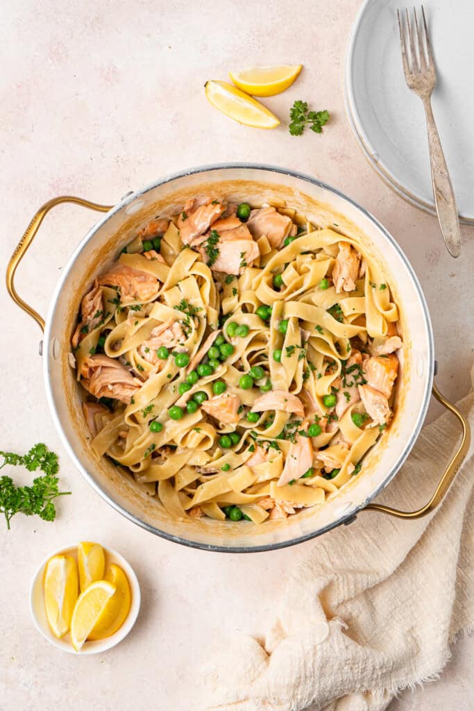 Dairy free creamy salmon tagliatelle in a pot with lemon and parsley to garnish.