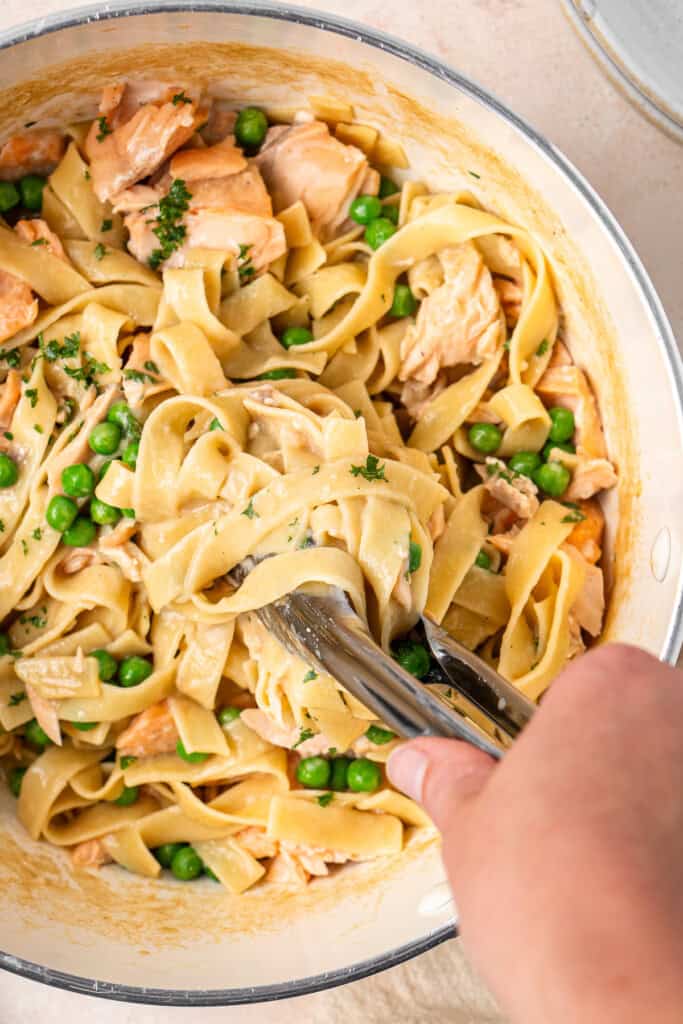 Mixing the flaked salmon and peas into the creamy pasta.