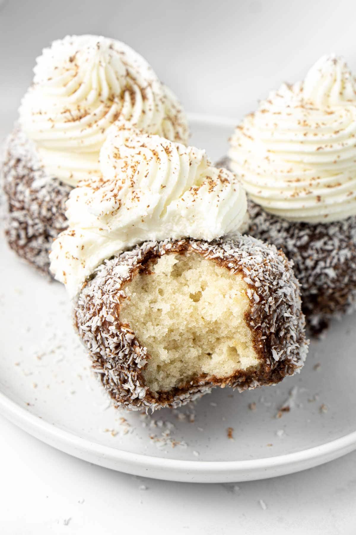 Close up of a lamington cupcake on a white plate with a bite taken from it.