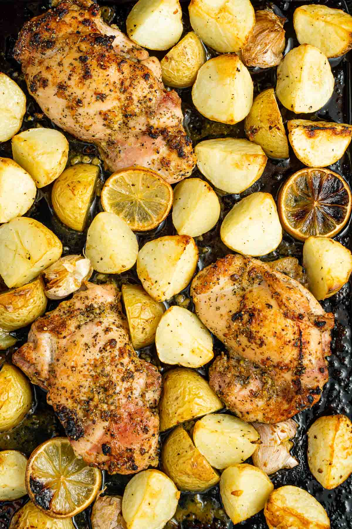 Close up of roasted chicken, potatoes and lemon on a baking tray.