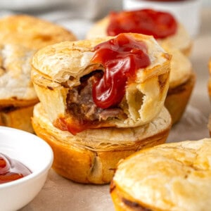 Mini beef pies stacked on top of each other with a bite taken and tomato sauce.