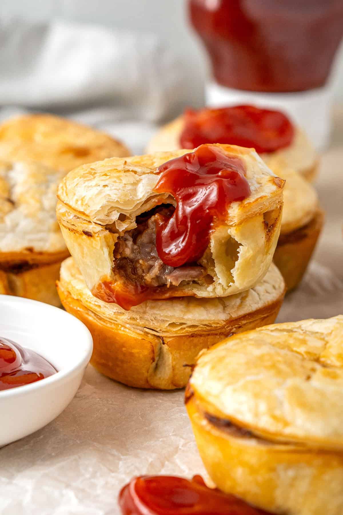 Mini beef pies stacked on top of each other with a bite taken and tomato sauce.