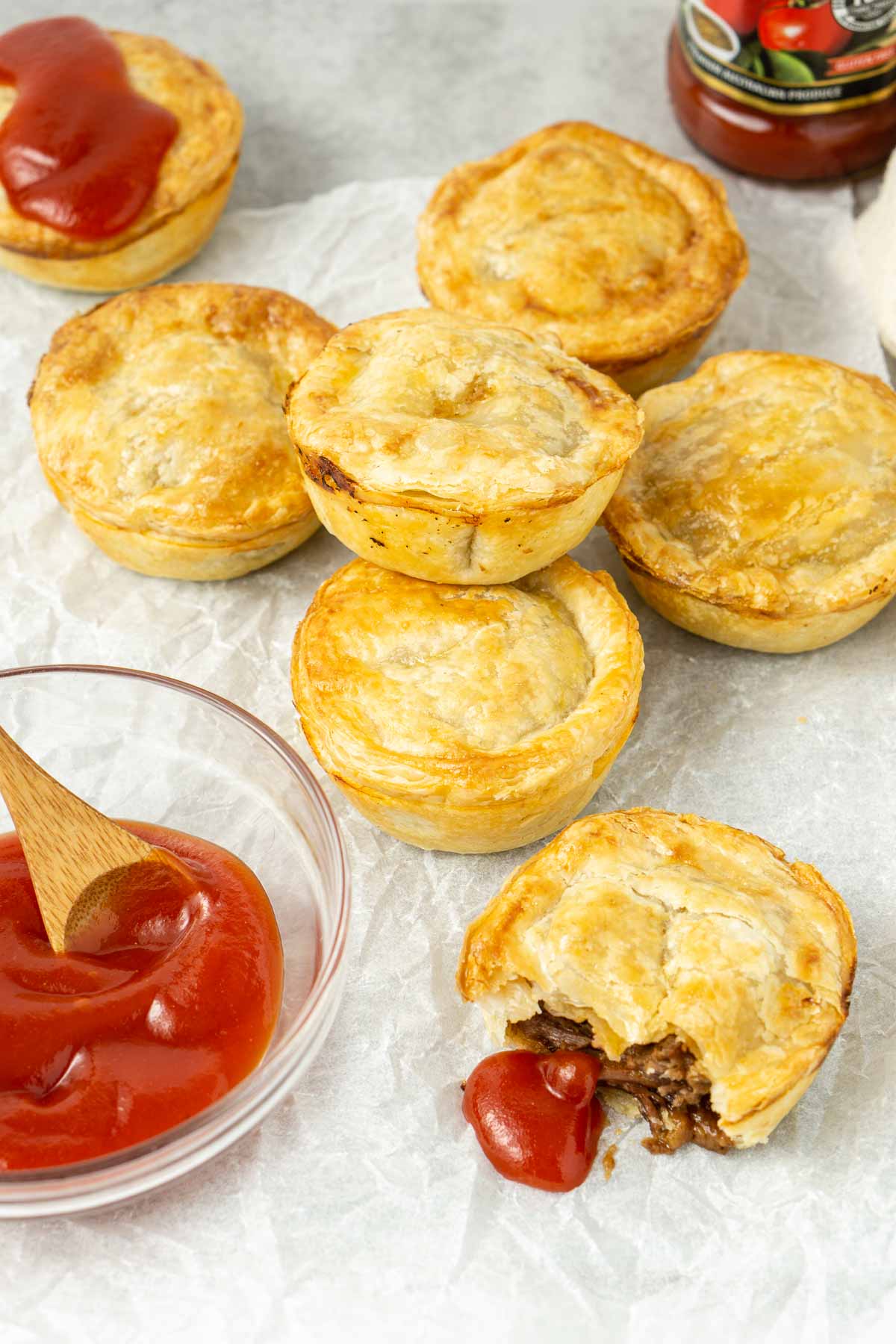 Mini beef pies laid out on baking paper with tomato sauce.