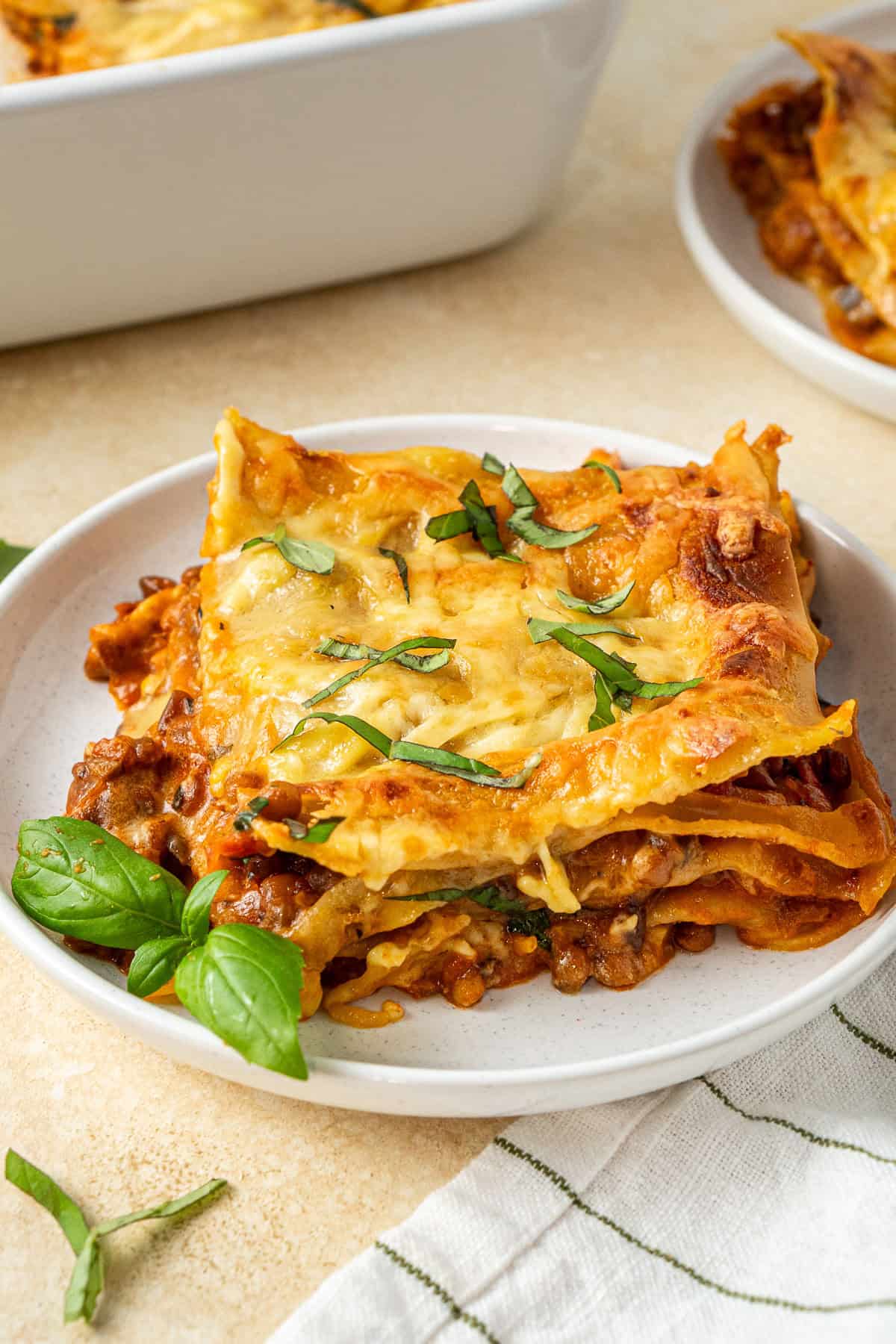 A slice of vegan lentil lasagne on a white plate with fresh basil.