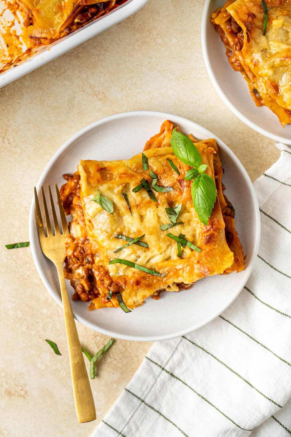 A slice of lasagne on a white plate with a gold fork.