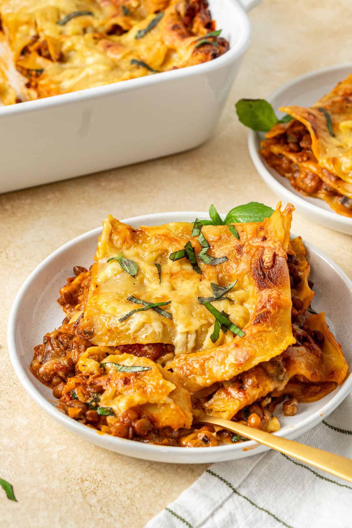 A slice of vegan lentil lasagne on a white plate with a gold fork.
