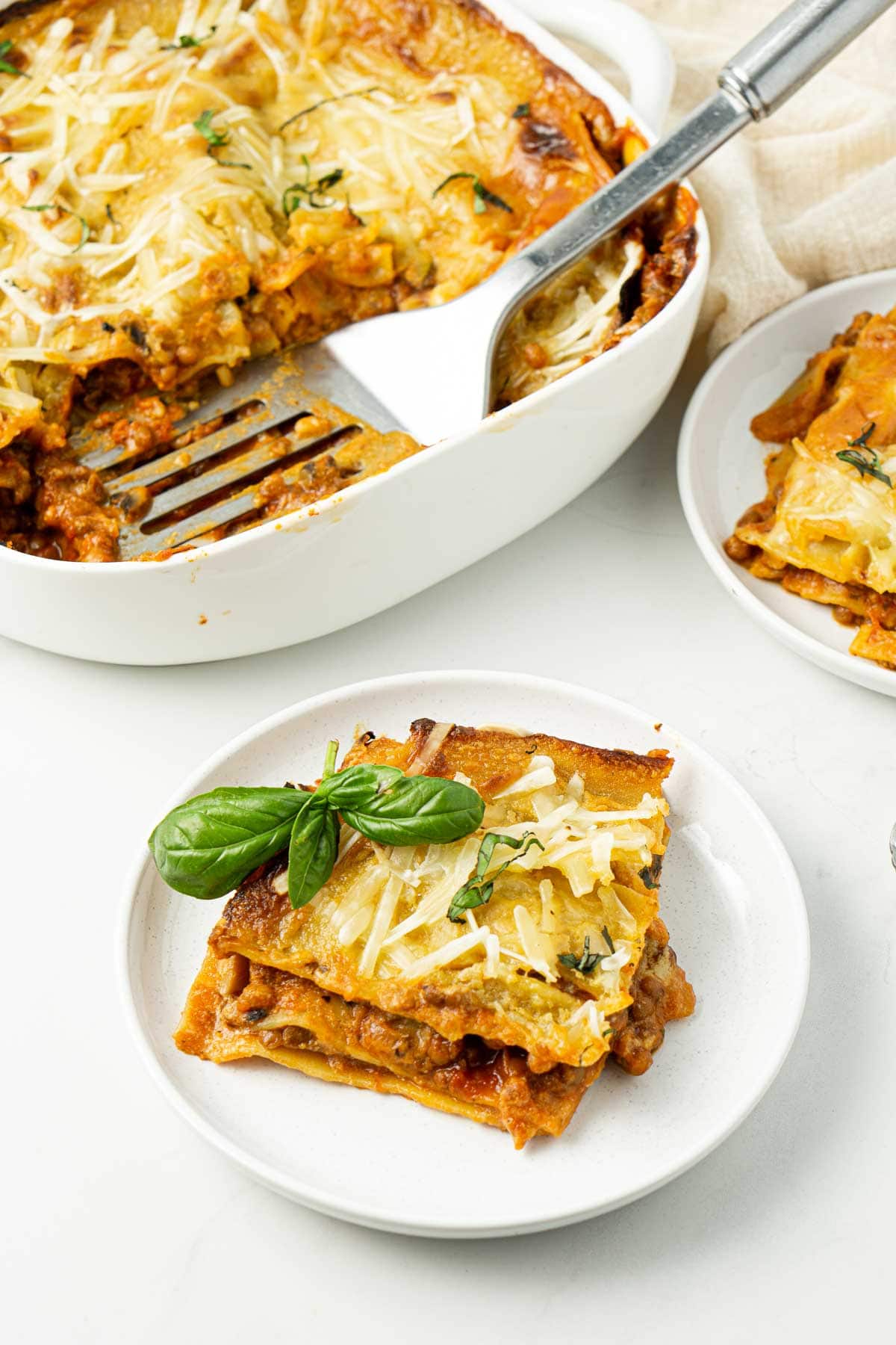 Vegan lentil lasagne cut into squares and served on white plates.