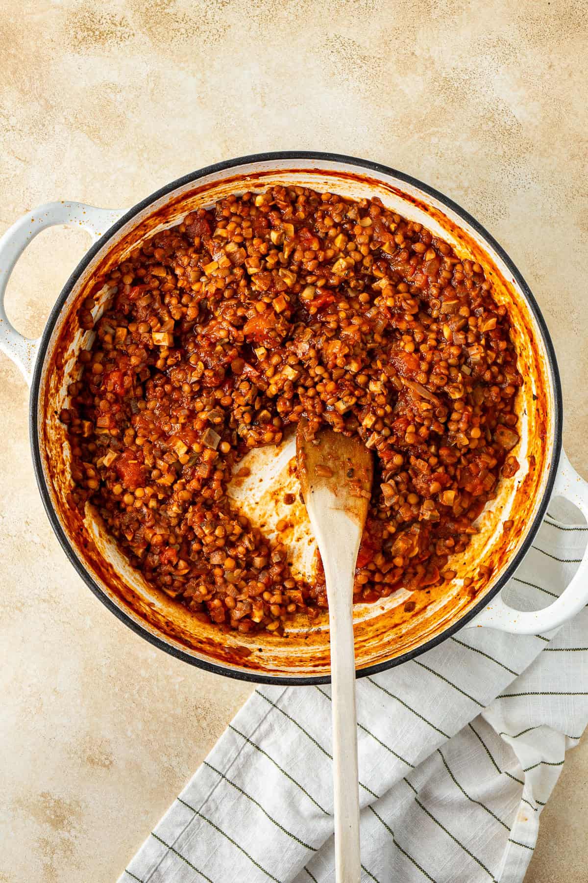 The cooked lentil tomato sauce in a pan with a wooden spoon.