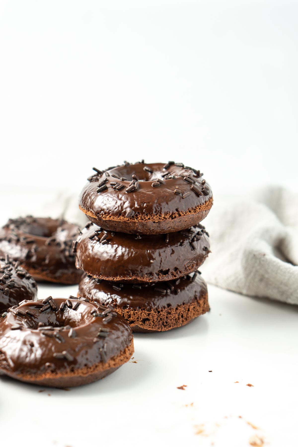 Three chocolate doughnuts with chocolate ganache stacked on top of each other. 