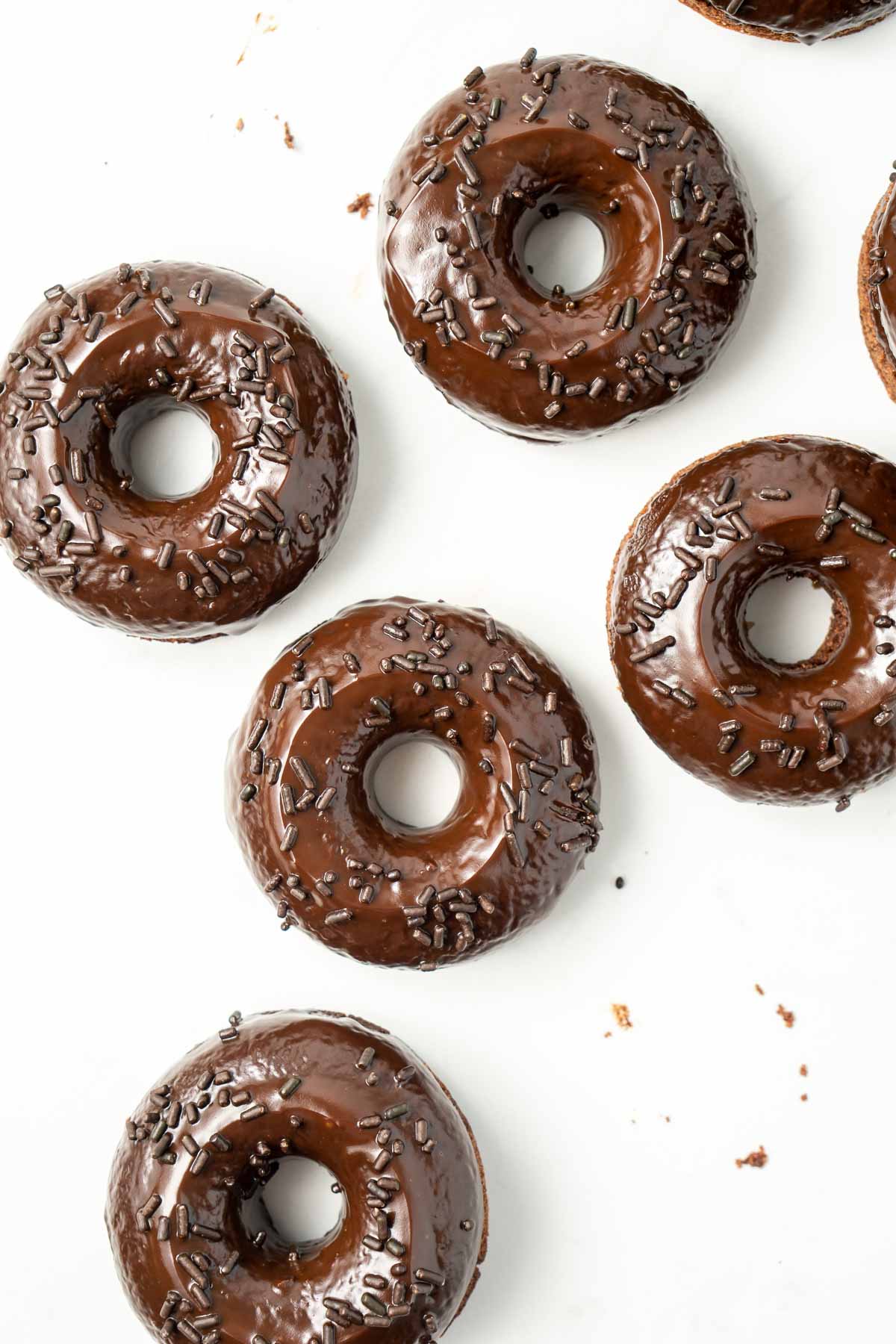 Six chocolate doughnuts with chocolate ganache and sprinkles from above, laid out on a white background.