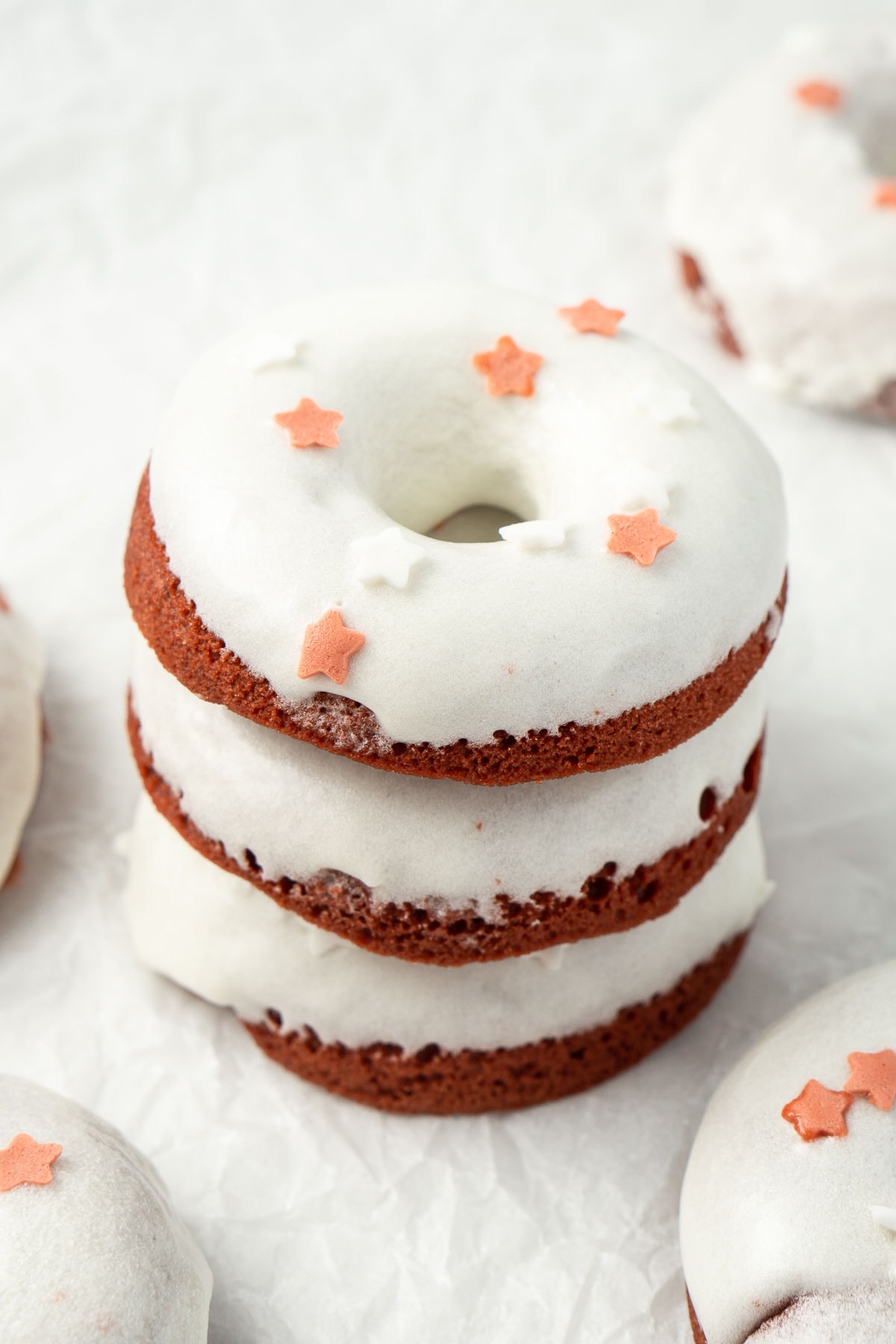 Red velvet doughnuts staked on top of each other with white cream cheese glaze and red and white sprinkles.