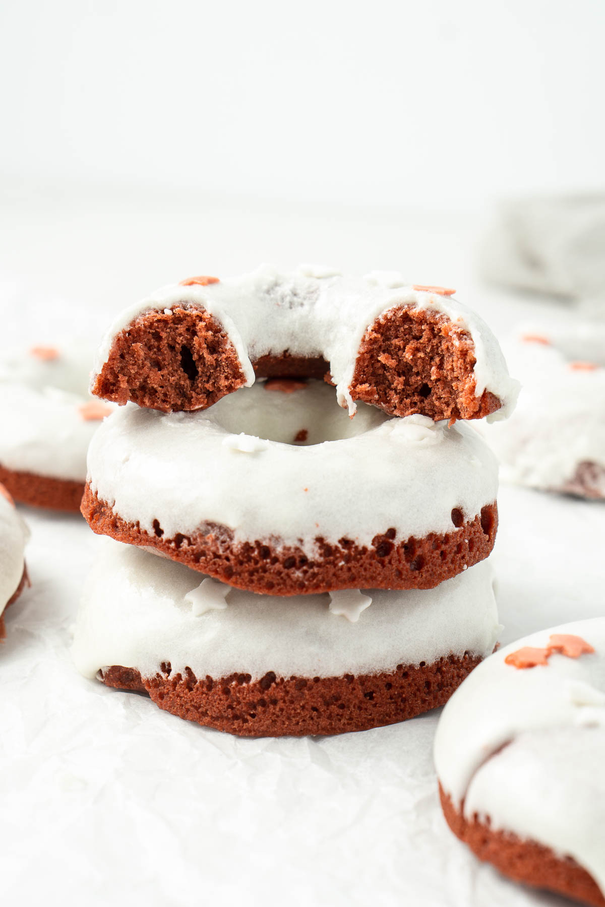 Red velvet doughnuts staked on top of each other with white cream cheese glaze and red and white sprinkles.