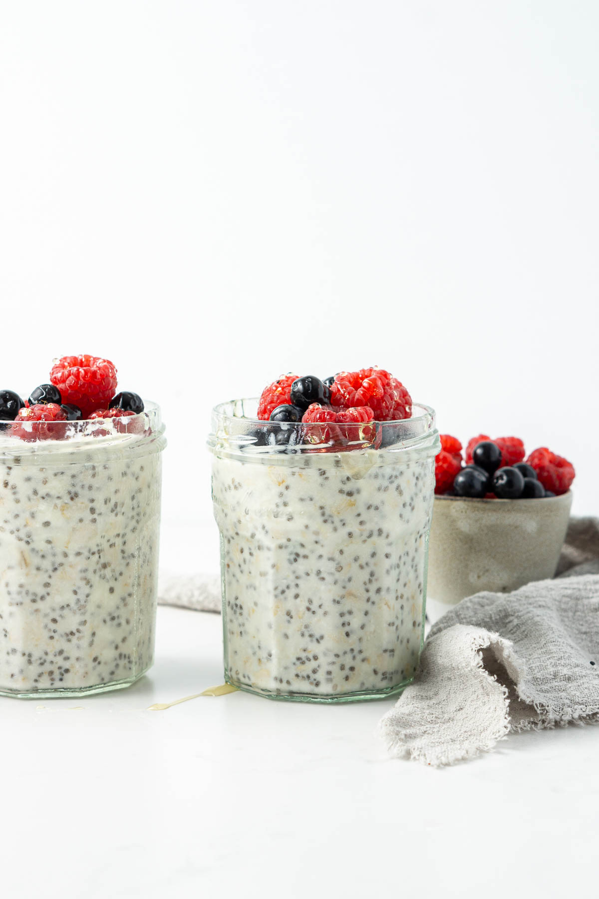 Side angle of 2 jars of vanilla overnight oats with berries and honey.
