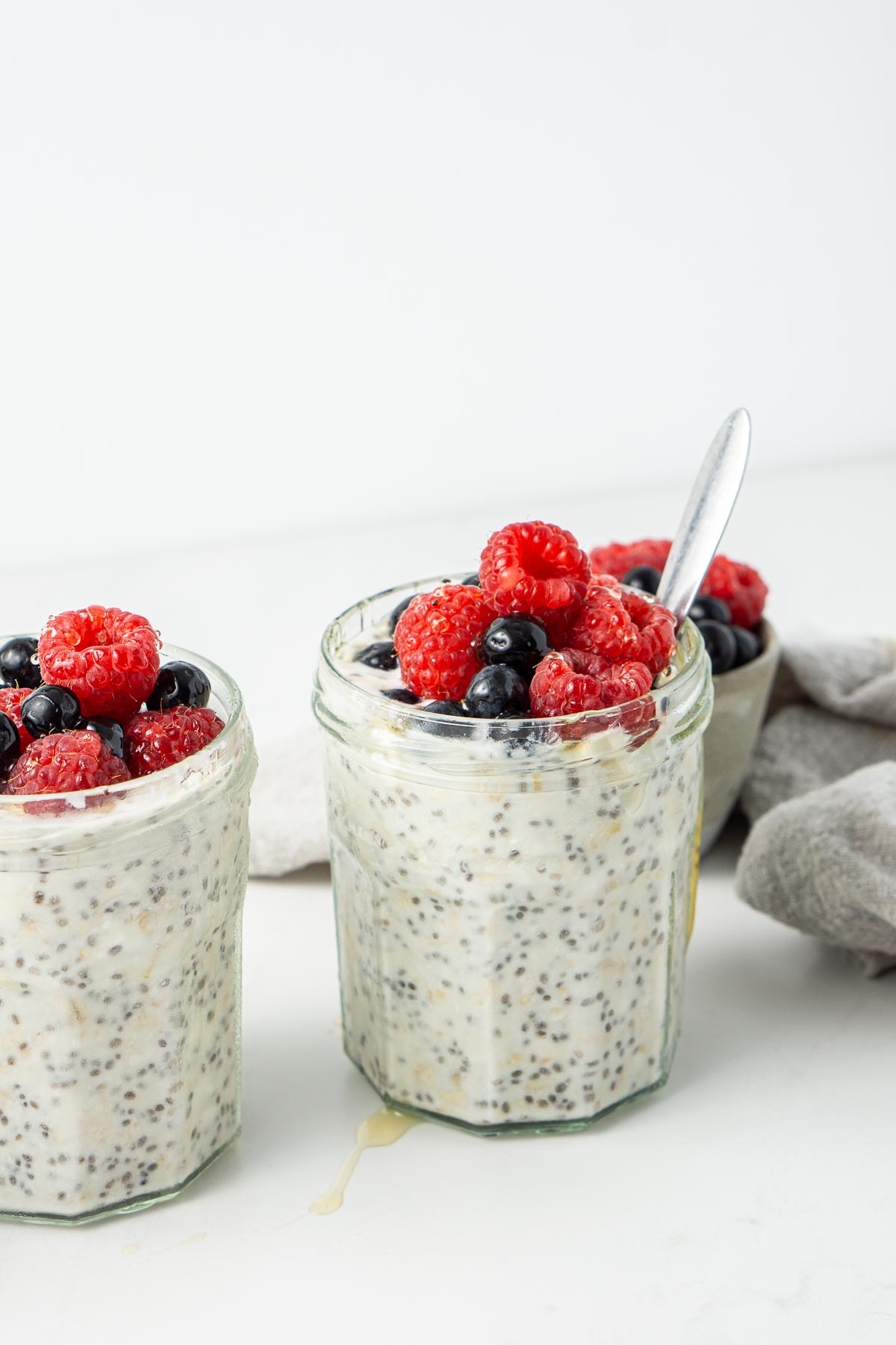 Overnight oats in jars topped with fresh berries and honey with a spoon.