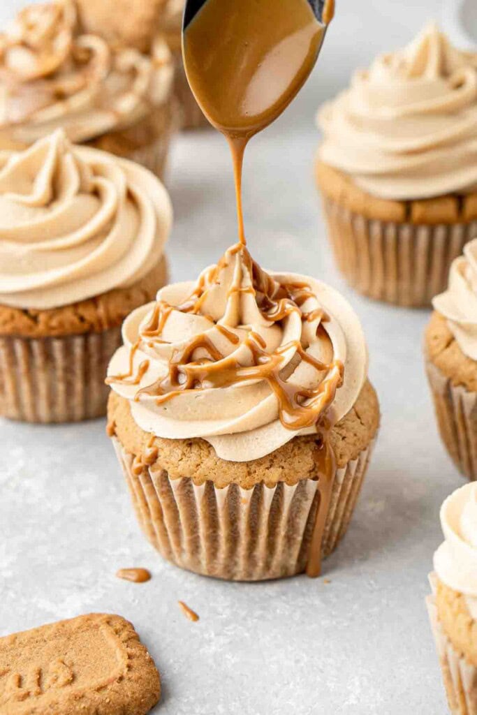 Spoon drizzling biscoff over the cupcakes.