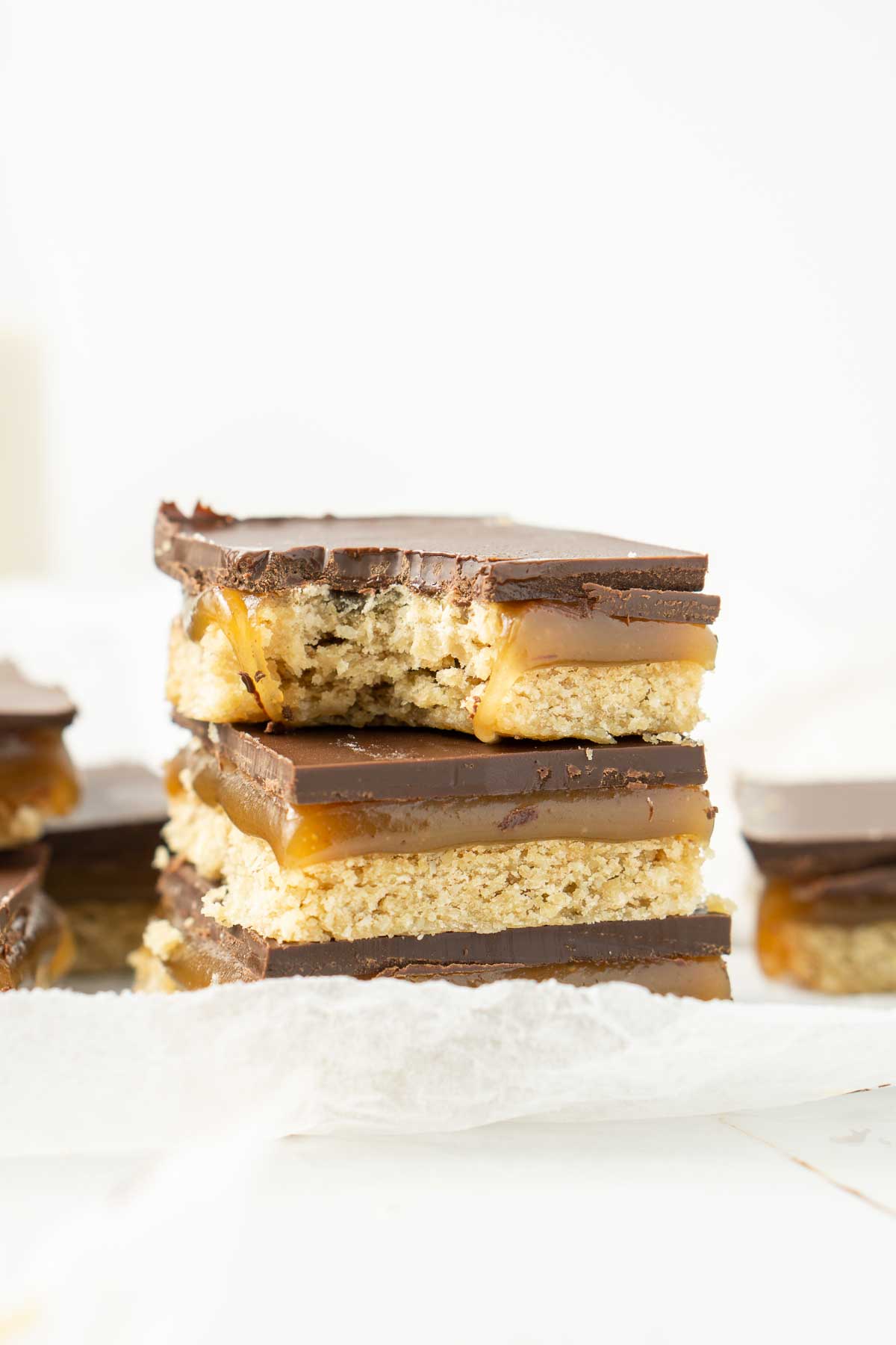 Close up of caramel slice on white baking paper with a bite taken.
