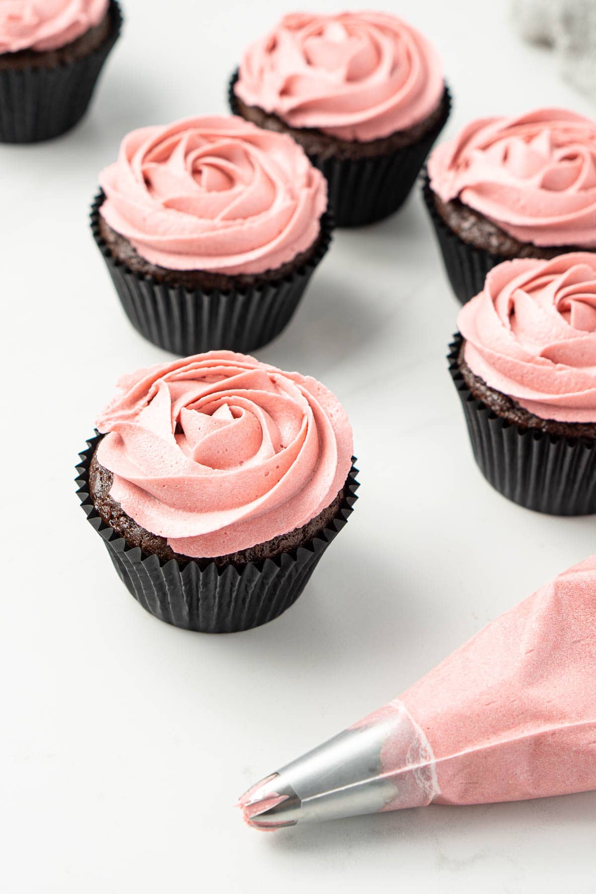 Chocolate cupcakes with a pink piped buttercream rose and piping bag with pink icing. 