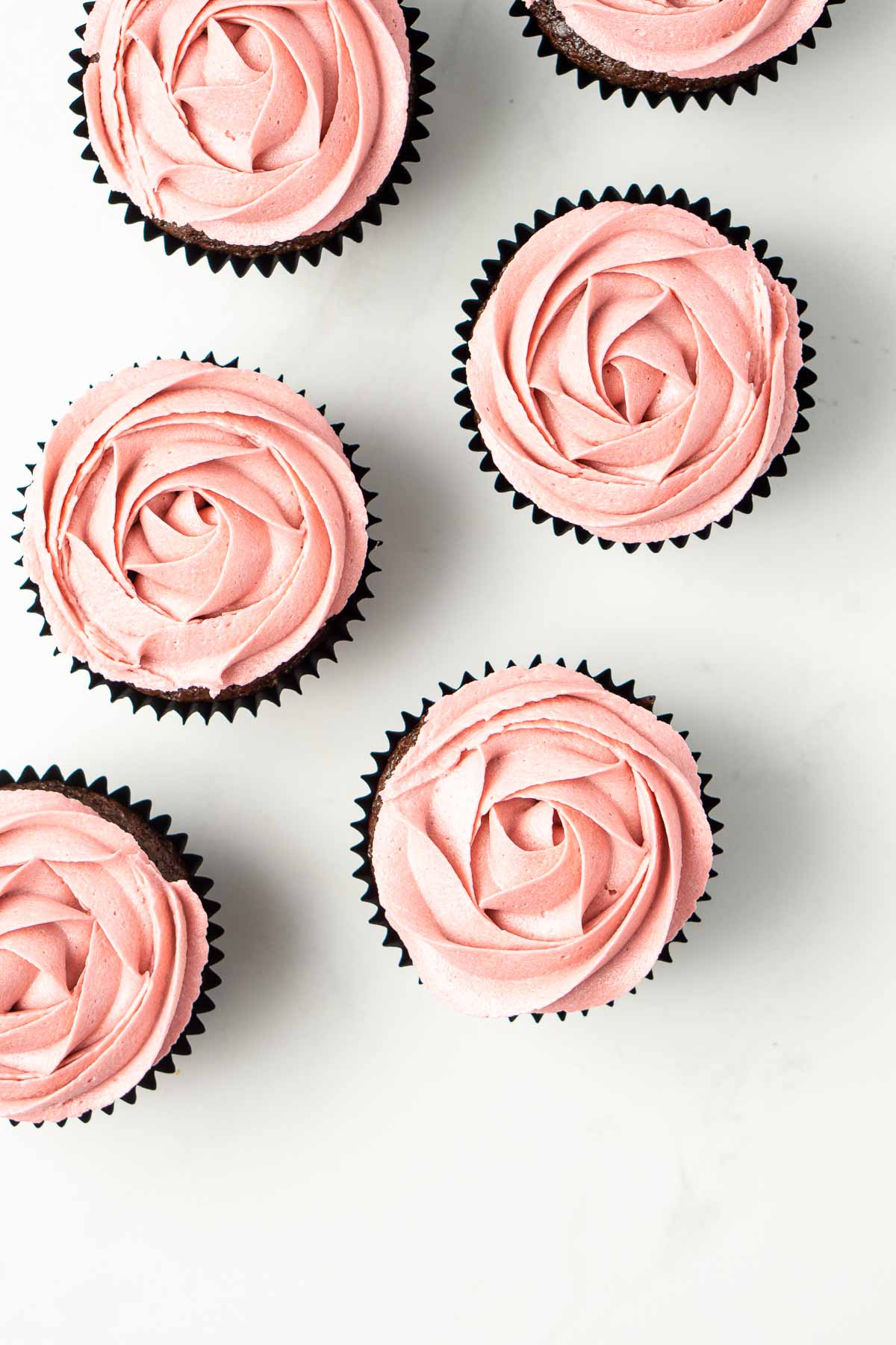 Overhead angle of chocolate cupcakes with pink vegan vanilla buttercream roses piped on top.