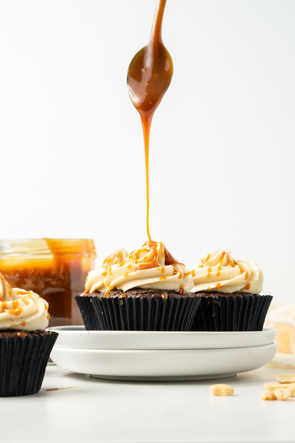 Large drizzle of caramel sauce on top of peanut butter frosted chocolate cupcakes.