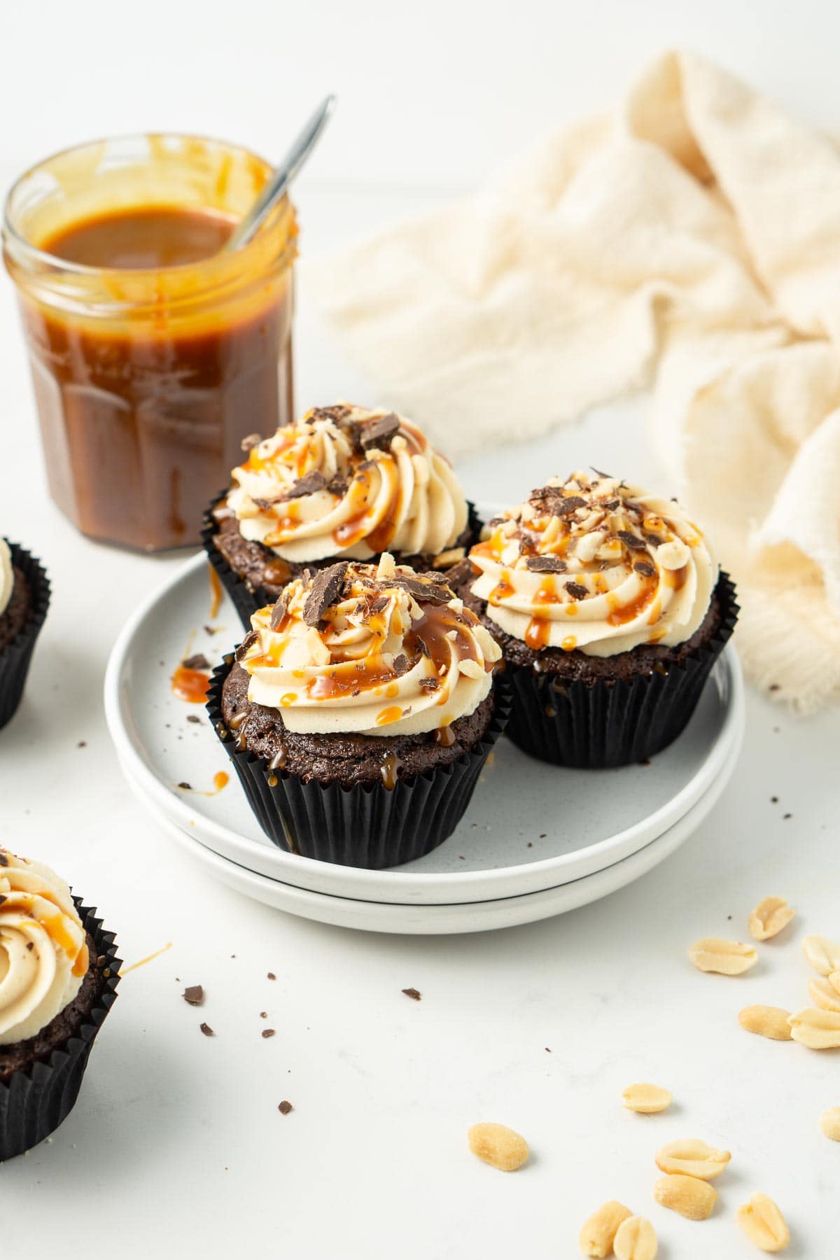 Three snickers cupcakes on a white plate with vegan caramel sauce.