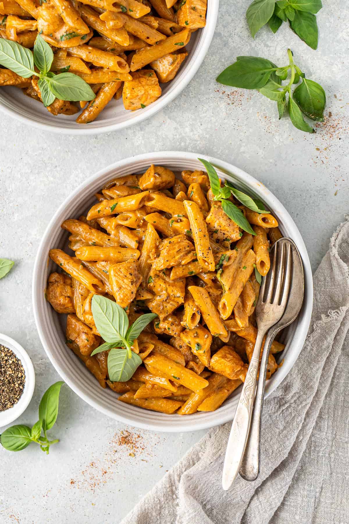 The creamy dairy free Cajun chicken pasta served into bowls with fresh basil and a spoon and fork.