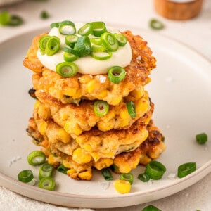 A stack of gluten free corn fritters on a plate with a fork served with spring onions and mayo.