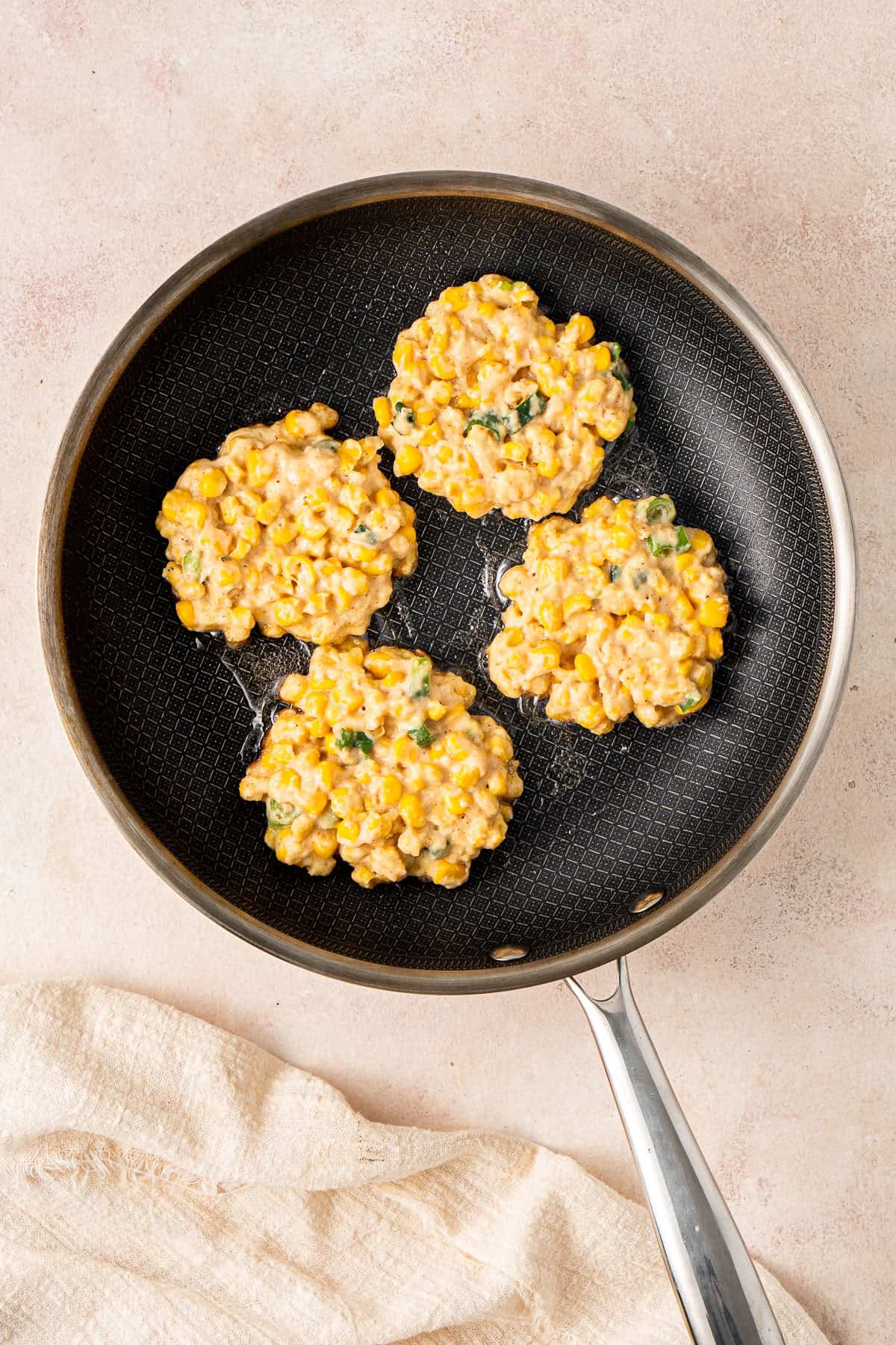 Four corn fritters in a frying pan with hot oil.