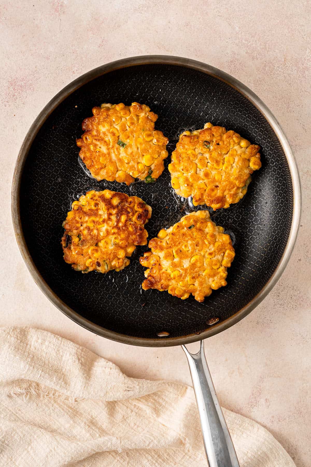 The corn fritters flipped and cooked in a frying pan.