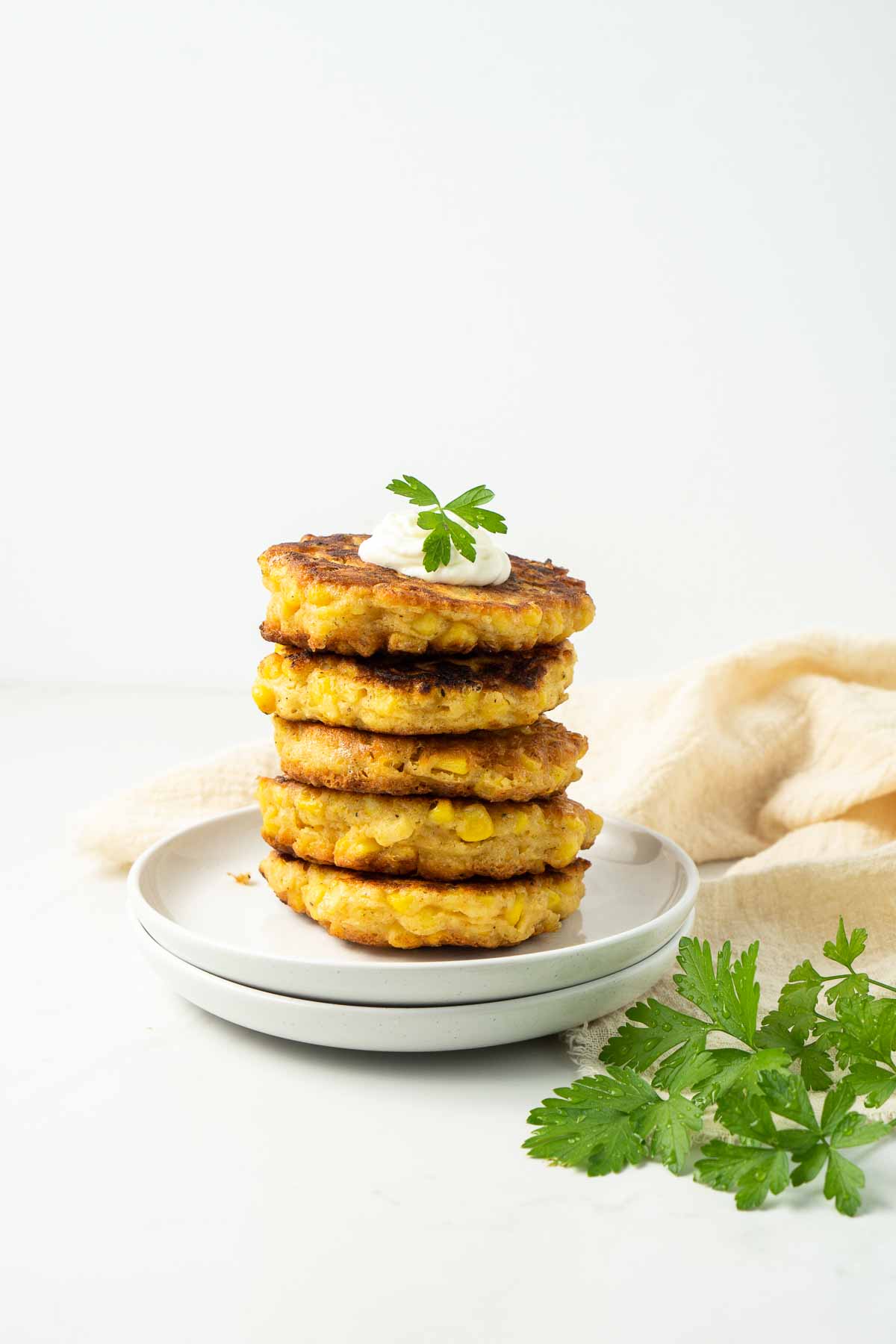 Stack of healthy corn fritters on 2 white plates with fresh parsley. 