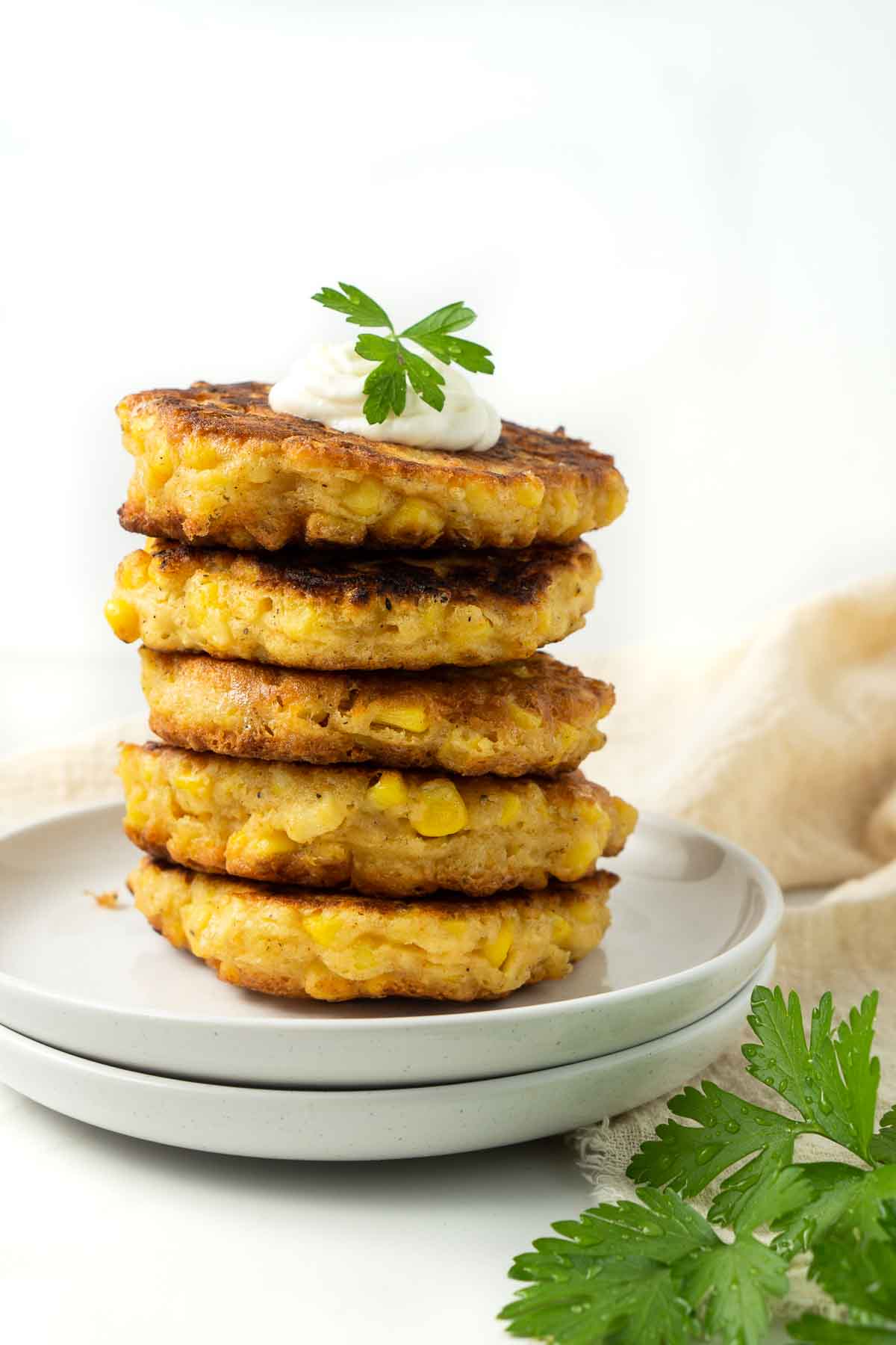 Close up of a stack of healthy corn fritters on 2 white plates with fresh parsley. 