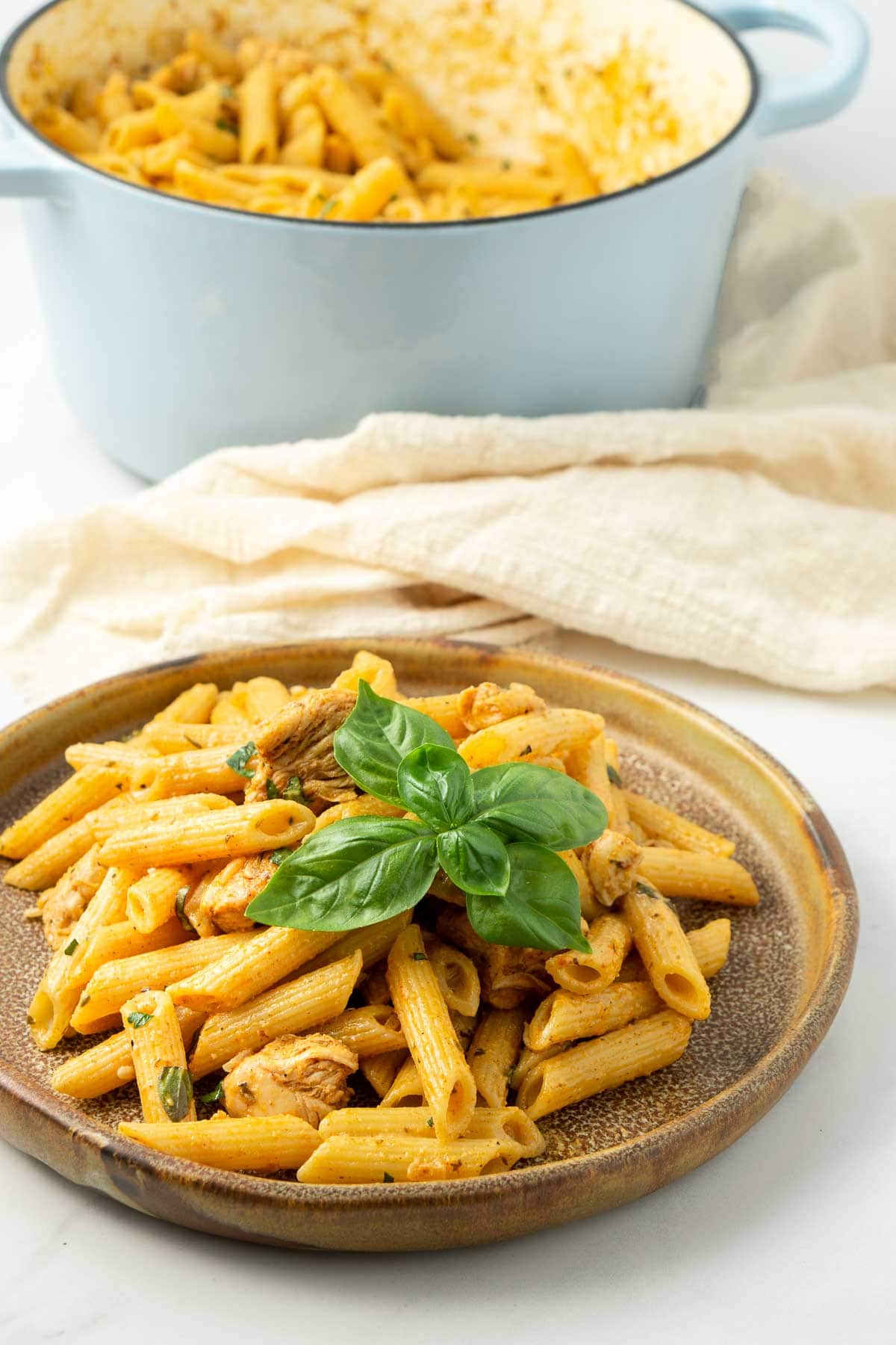 Cajun chicken pasta served on a plate with fresh basil and the large pot in the background.