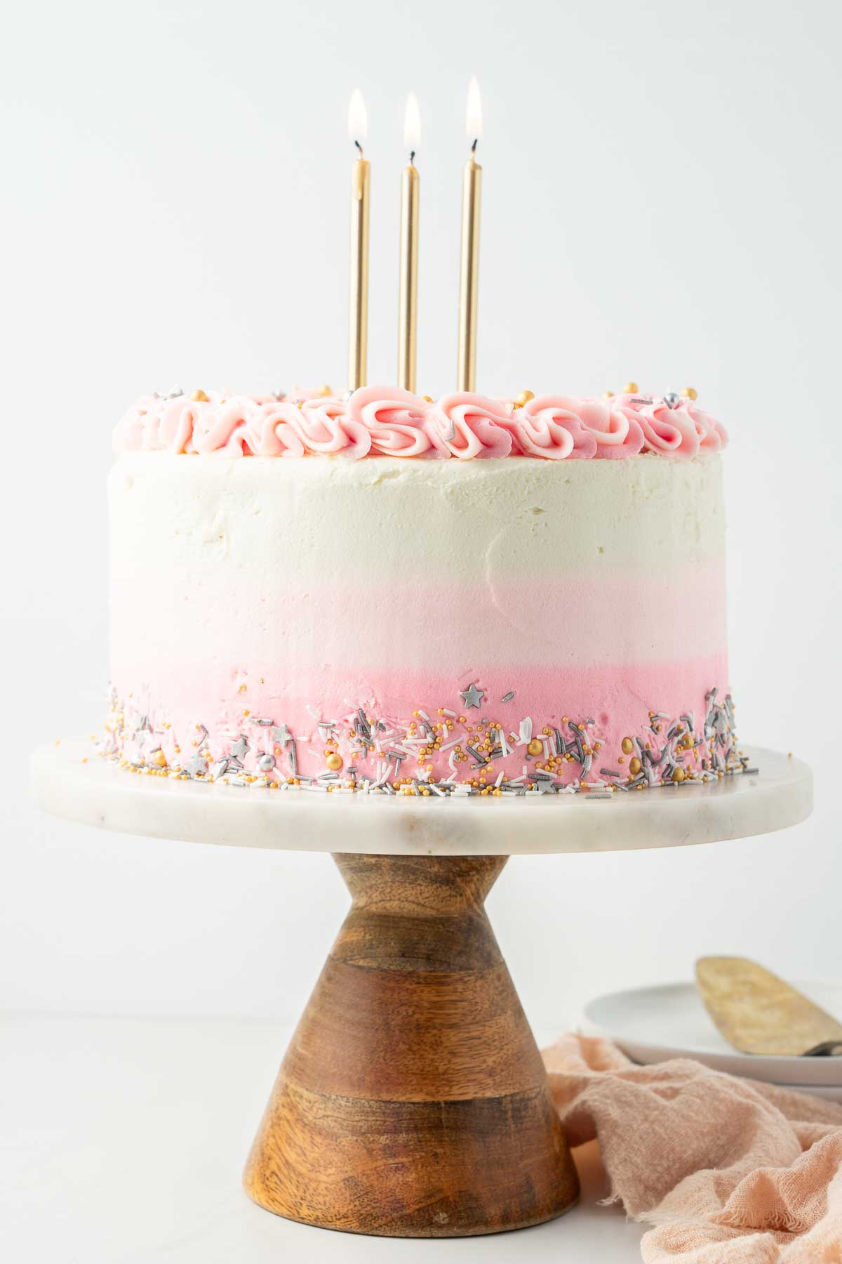 Vegan birthday cake with gold candles on a marble and wood cake stand. 