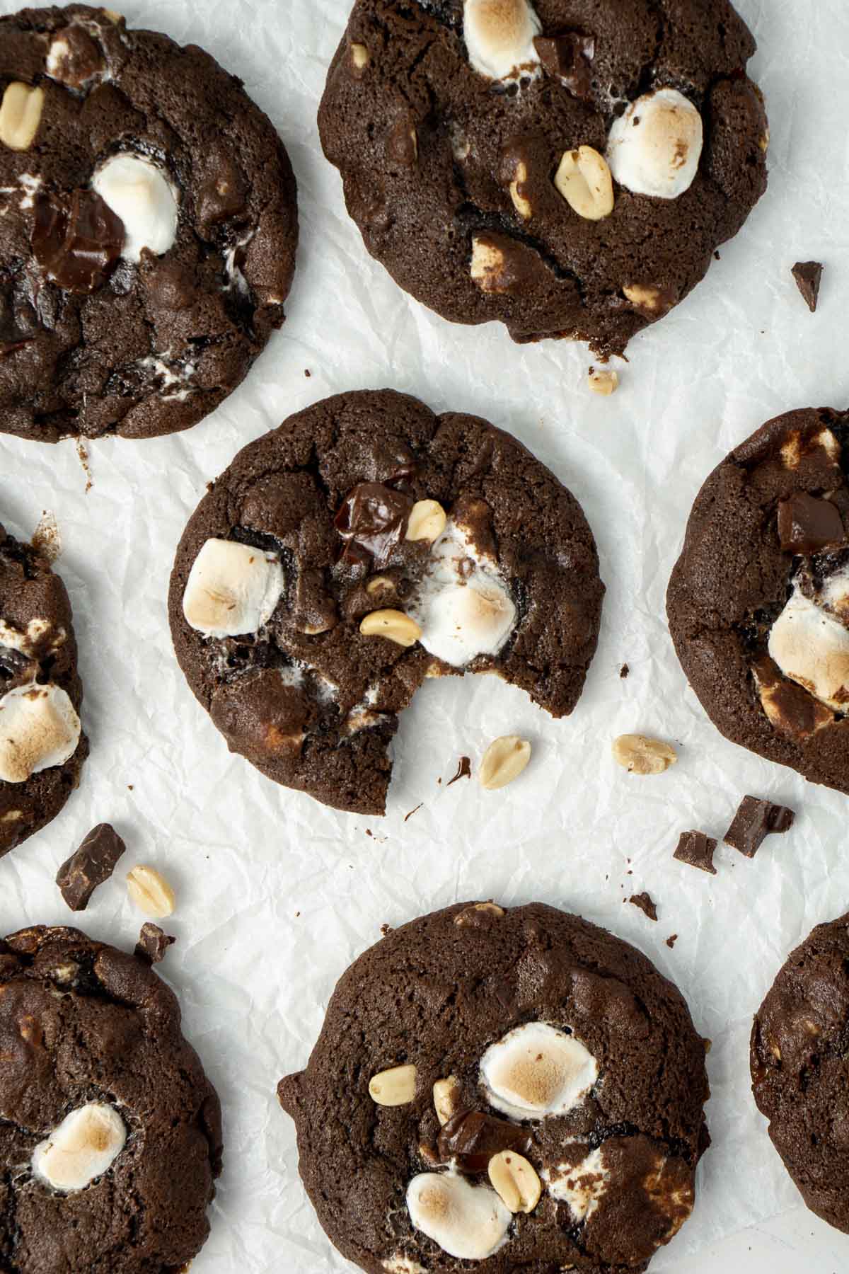 Rocky road cookies on baking paper, one with a bite taken.