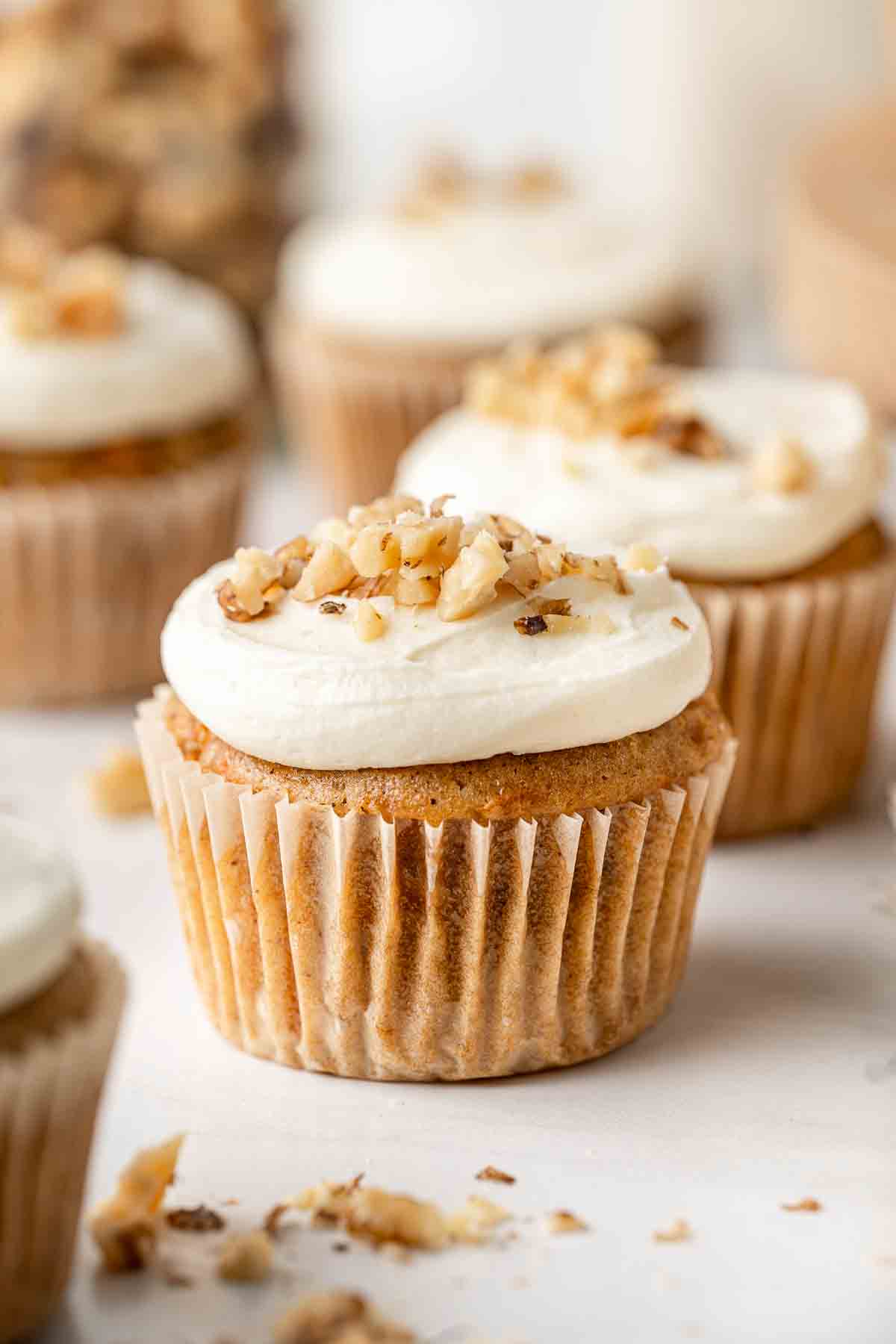 Close up of a vegan carrot cake cupcake topped with cream cheese frosting and crushed walnuts.