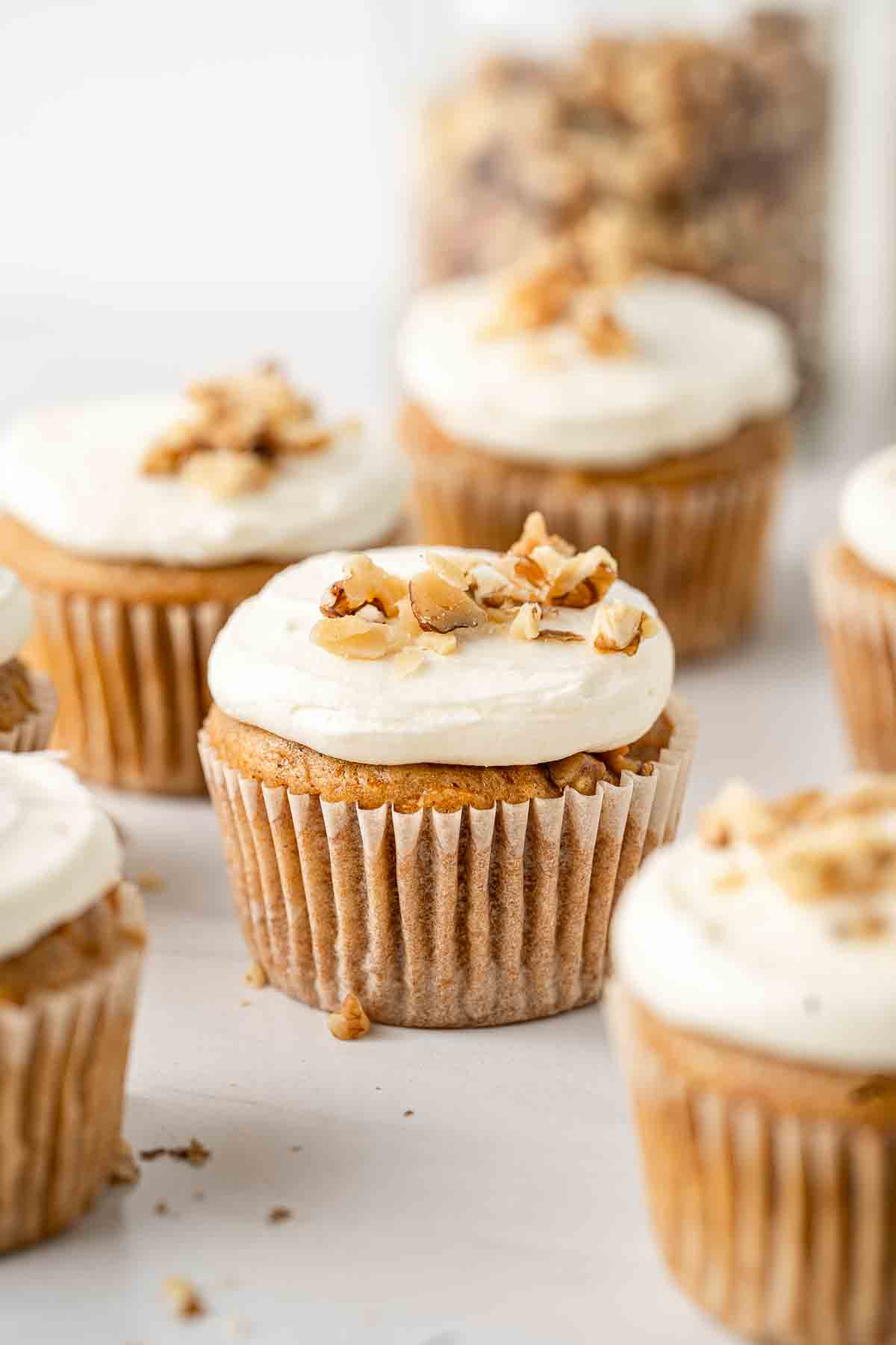 Vegan carrot cake cupcakes topped with cream cheese frosting and crushed walnuts.