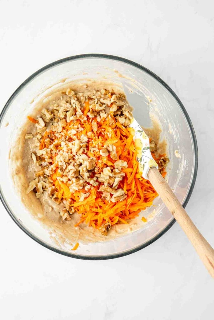 Adding the carrots and walnuts to the cupcake batter in a bowl.