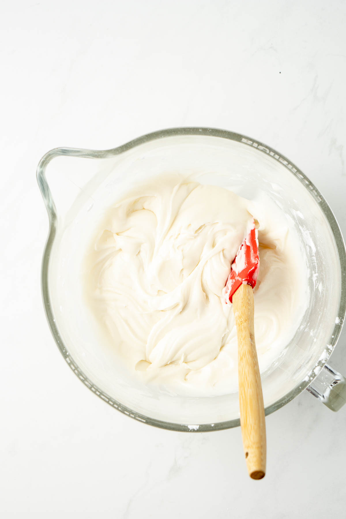 Glass bowl of cream cheese frosting with a rubber spatula. 